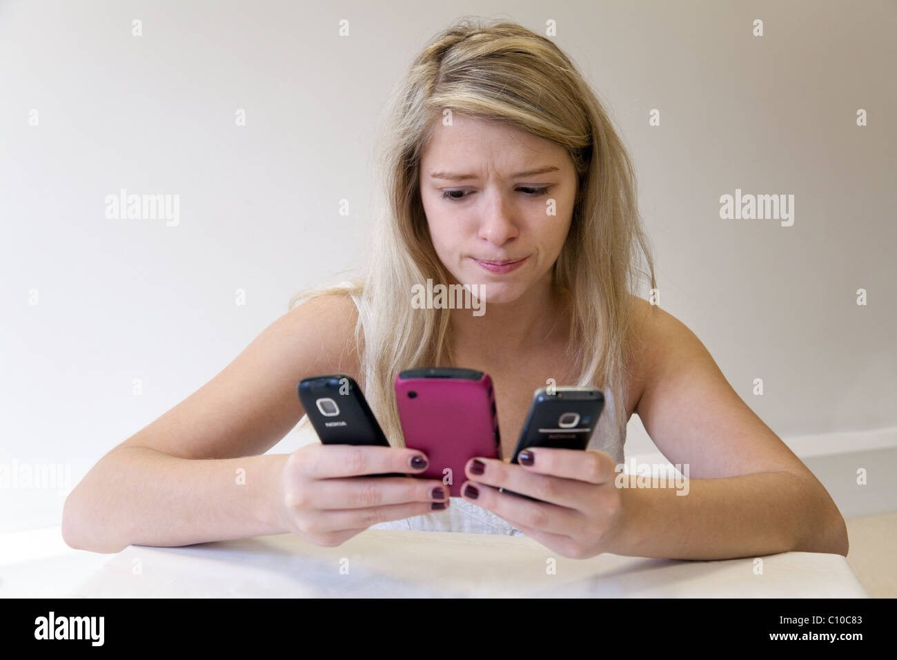 La bionda ragazza adolescente di detenzione e guardando 3 telefoni cellulari Foto Stock