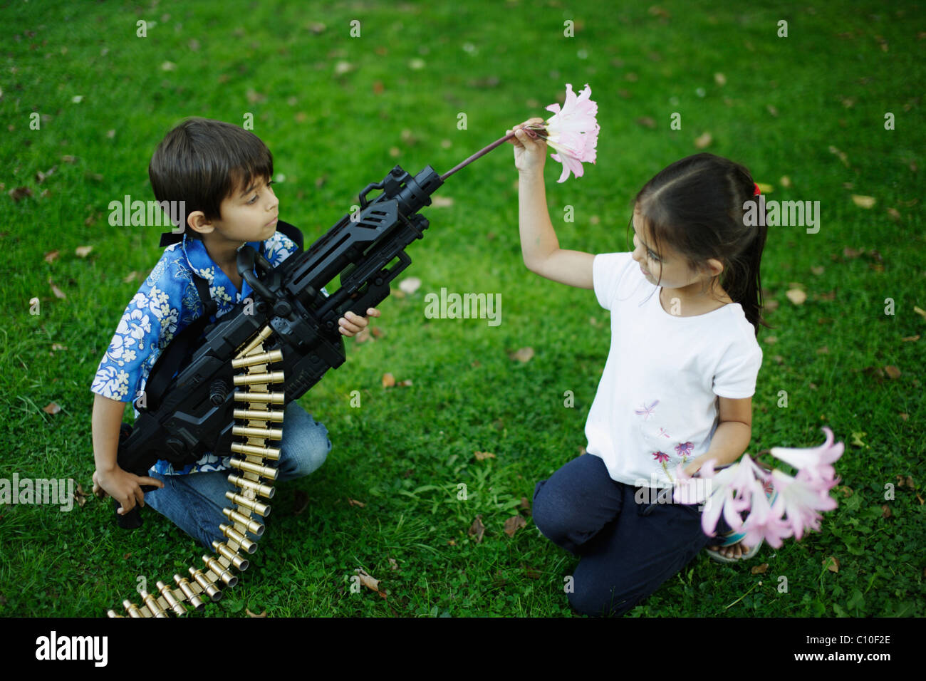 Bambina di cinque anni i luoghi dei fiori in camera di suo fratello's toy machine gun Foto Stock