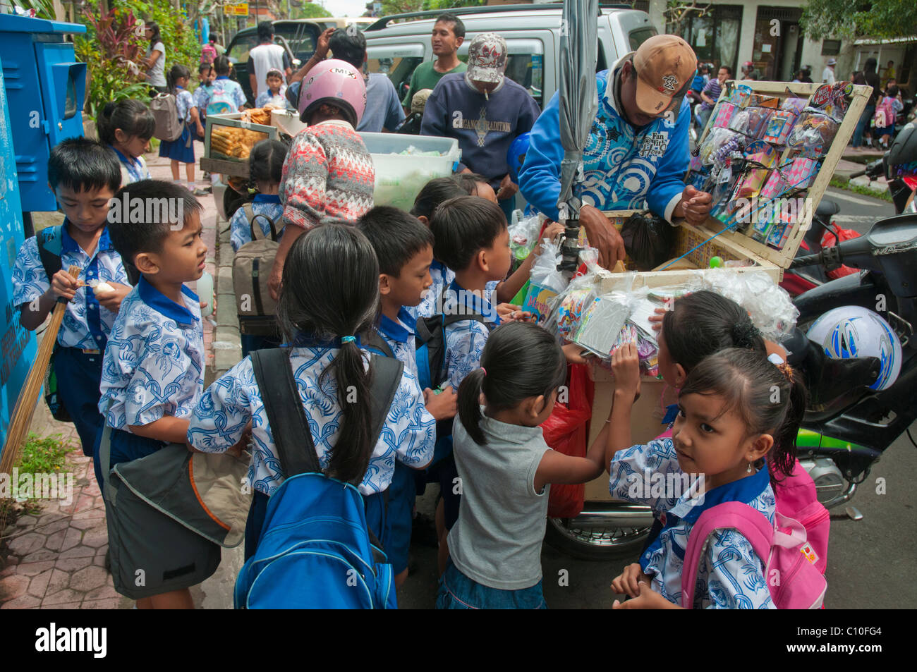 Indonesiano scuola primaria di acquisto i bambini dopo la scuola tratta da un venditore ambulante al di fuori della loro scuola in Ubud, Bali, Indonesia Foto Stock