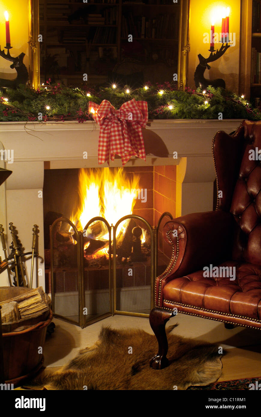 Nobile caminetto con fuoco ardente in una raffinata atmosfera, sedia in pelle e decorazione di Natale Foto Stock
