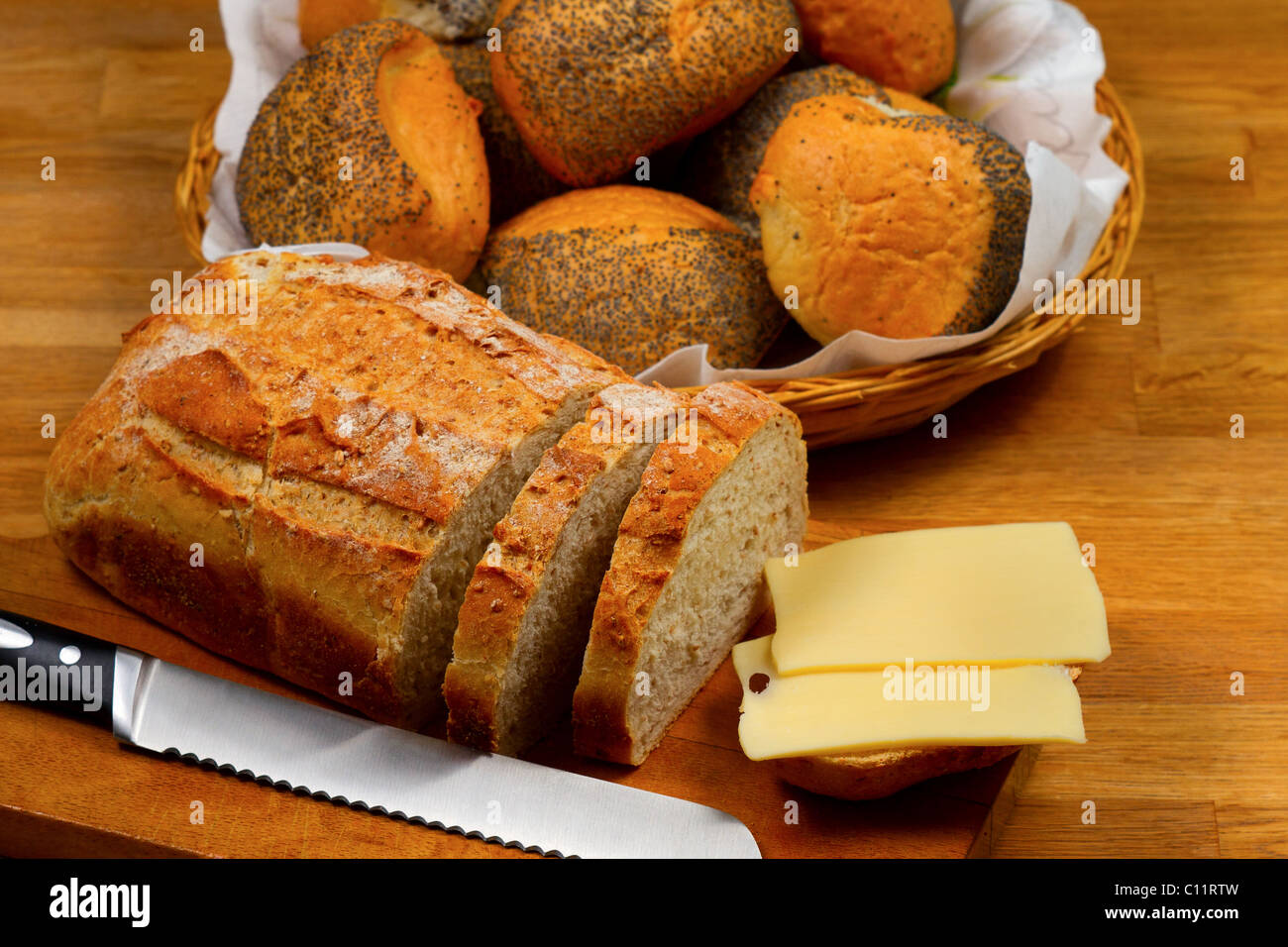 Pane fresco formaggio e il coltello sul tagliere di legno con cesto con pane in background Foto Stock