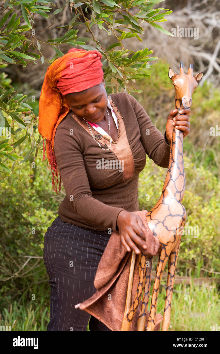 Donna di pulizia di una giraffa di legno, souvenir, il Capo di Buona Speranza, Western Cape vicino a Città del Capo, Penisola del Capo, in Sud Africa e Africa Foto Stock