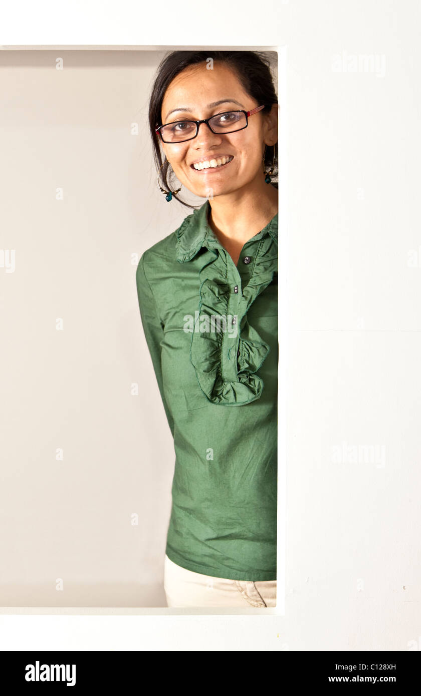 Sorridente donna indiana in corrispondenza della finestra, verde giada superiore e luce indossa i pantaloni glaases Foto Stock