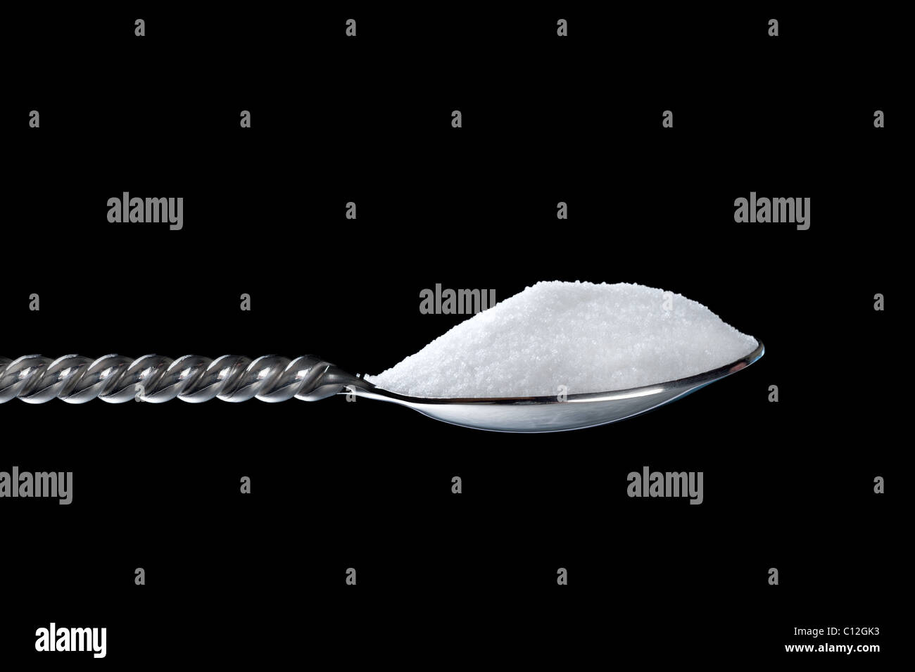 Un cucchiaio di zucchero semolato su uno sfondo nero. Foto Stock
