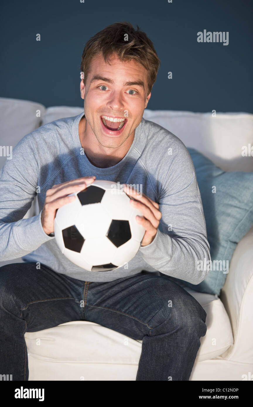 Metà uomo adulto seduto sul divano tenendo palla calcio e guardare la tv Foto Stock