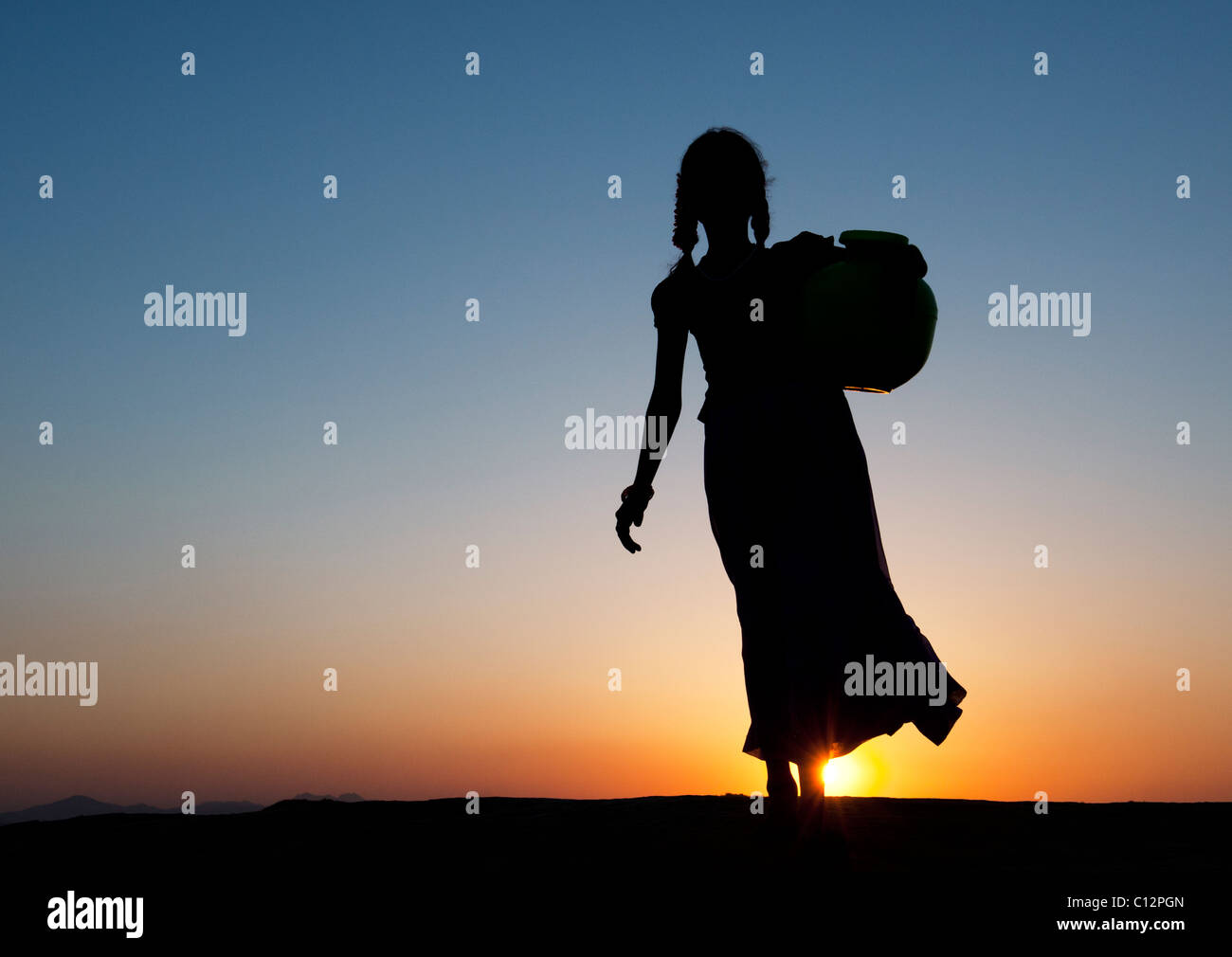 Rurale villaggio indiano ragazza camminare con acqua pot al tramonto. Silhouette. Andhra Pradesh, India Foto Stock