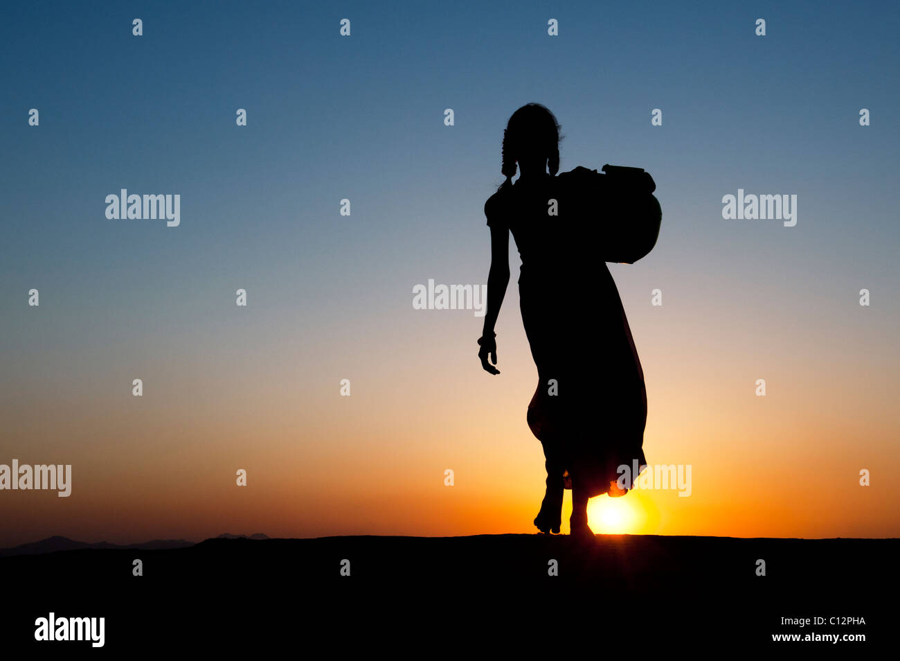 Rurale villaggio indiano ragazza camminare con acqua pot al tramonto. Silhouette. Andhra Pradesh, India Foto Stock