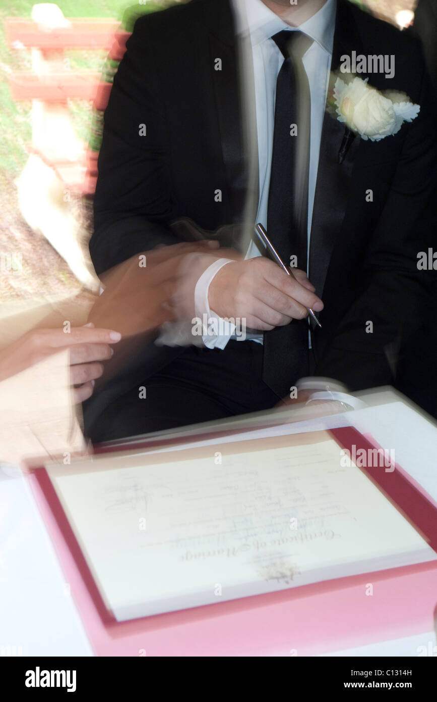 Lo sposo firma il certificato di matrimonio guidato da sposa Foto Stock