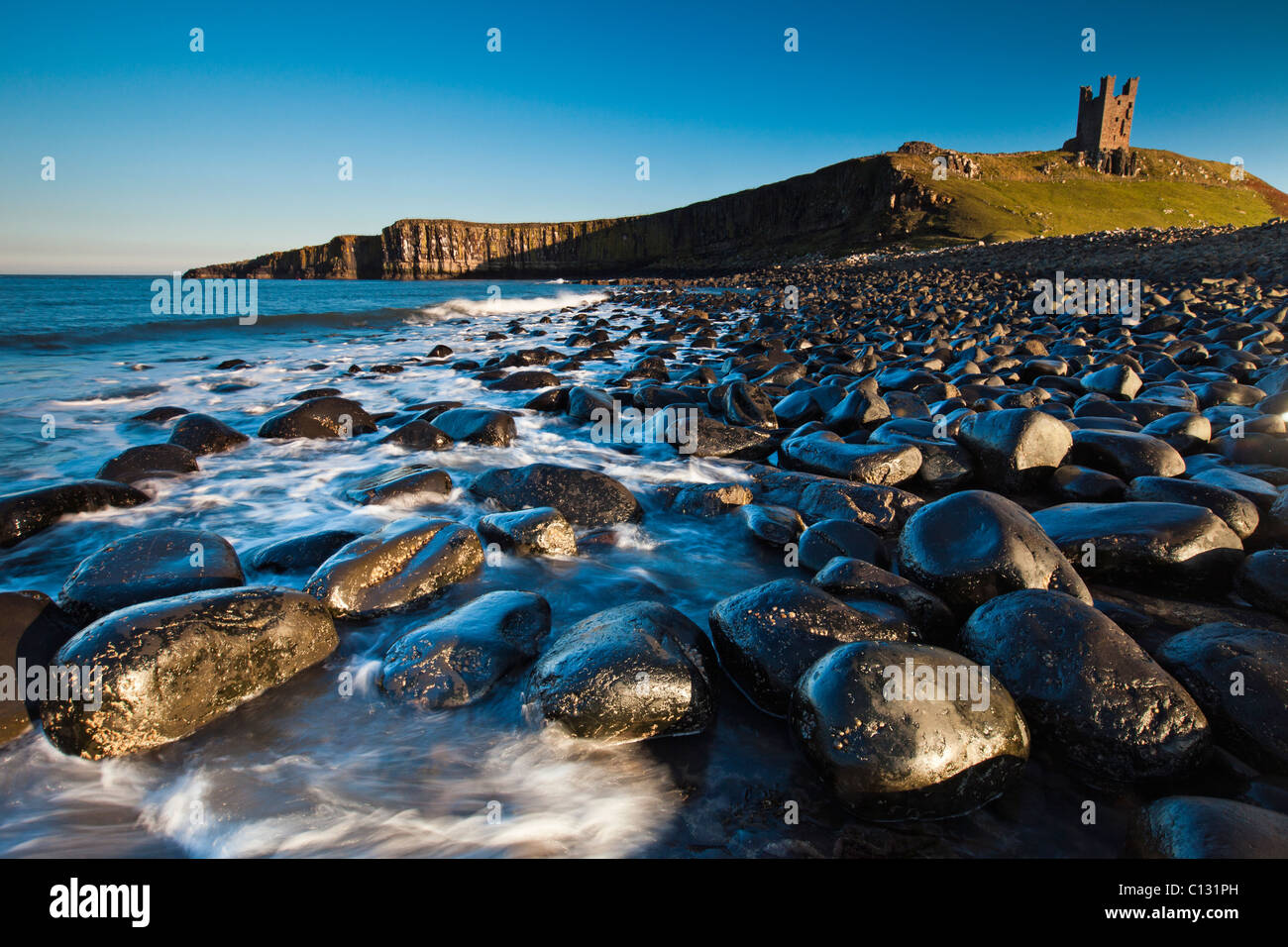 Il castello di Dunstanburgh, con massi di basalto sulla spiaggia, autunno, Northumberland, Inghilterra Foto Stock