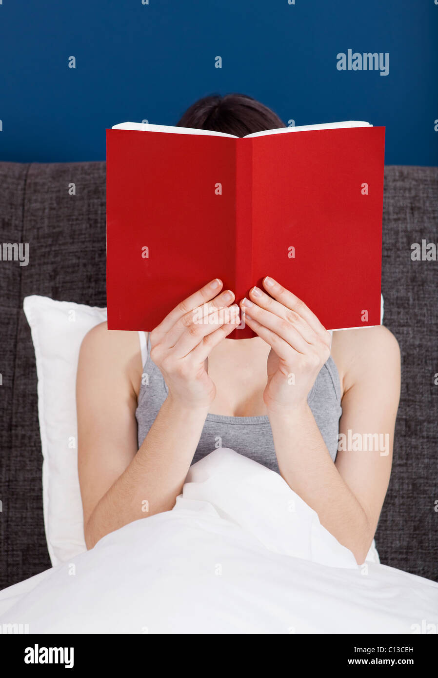 Donna che legge un libro con la faccia coperta dal libro Foto Stock
