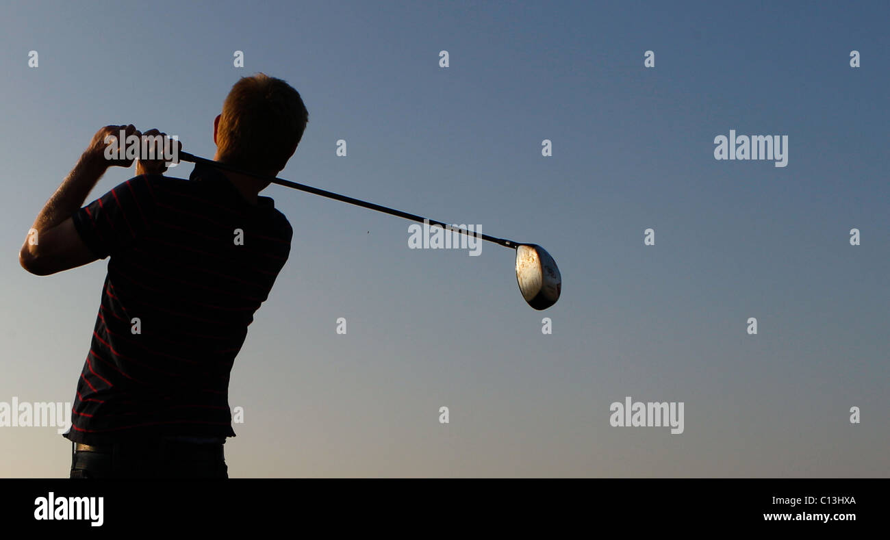 L uomo per giocare a golf con un paesaggio panoramico intorno a lui come il sole tramonta Foto Stock