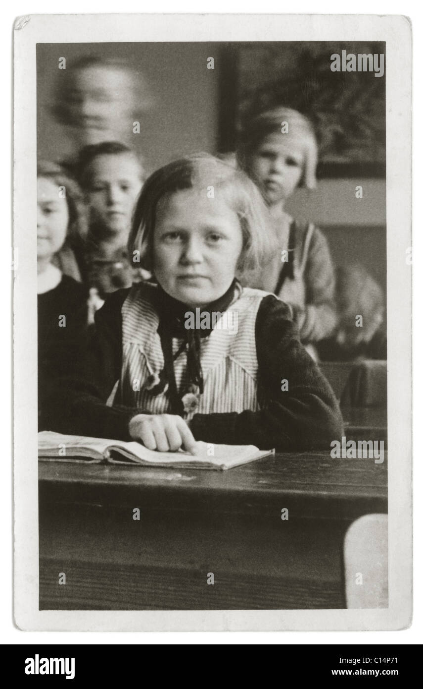 Schoolgirl seduto alla sua scrivania con un libro in una scuola primaria - classe 1930, U.K. Foto Stock