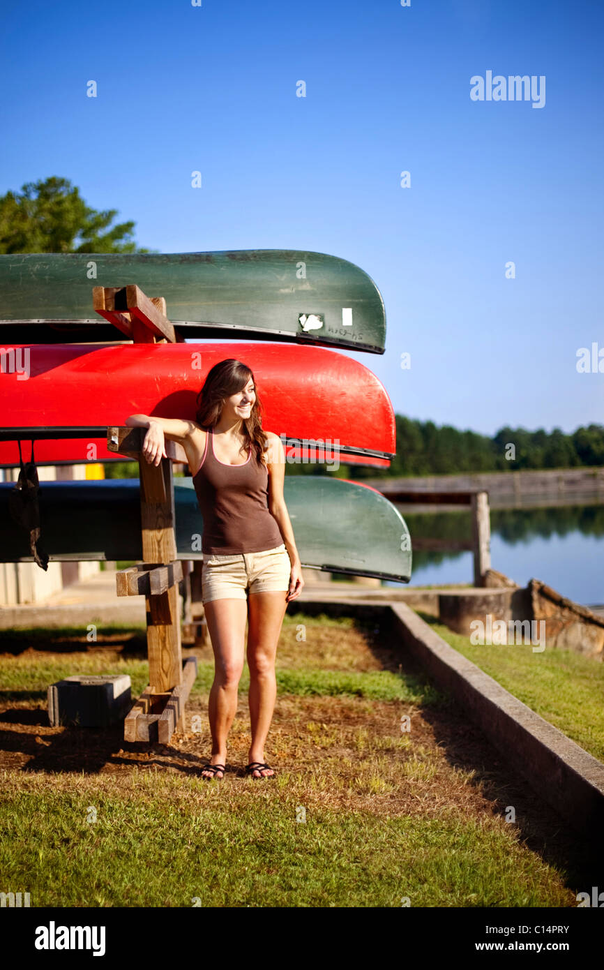 Giovane donna appoggiando se stessa da una cremagliera di canoe guardando fuori sull'acqua. Oak Mountain State Park, Pelham, AL. Foto Stock