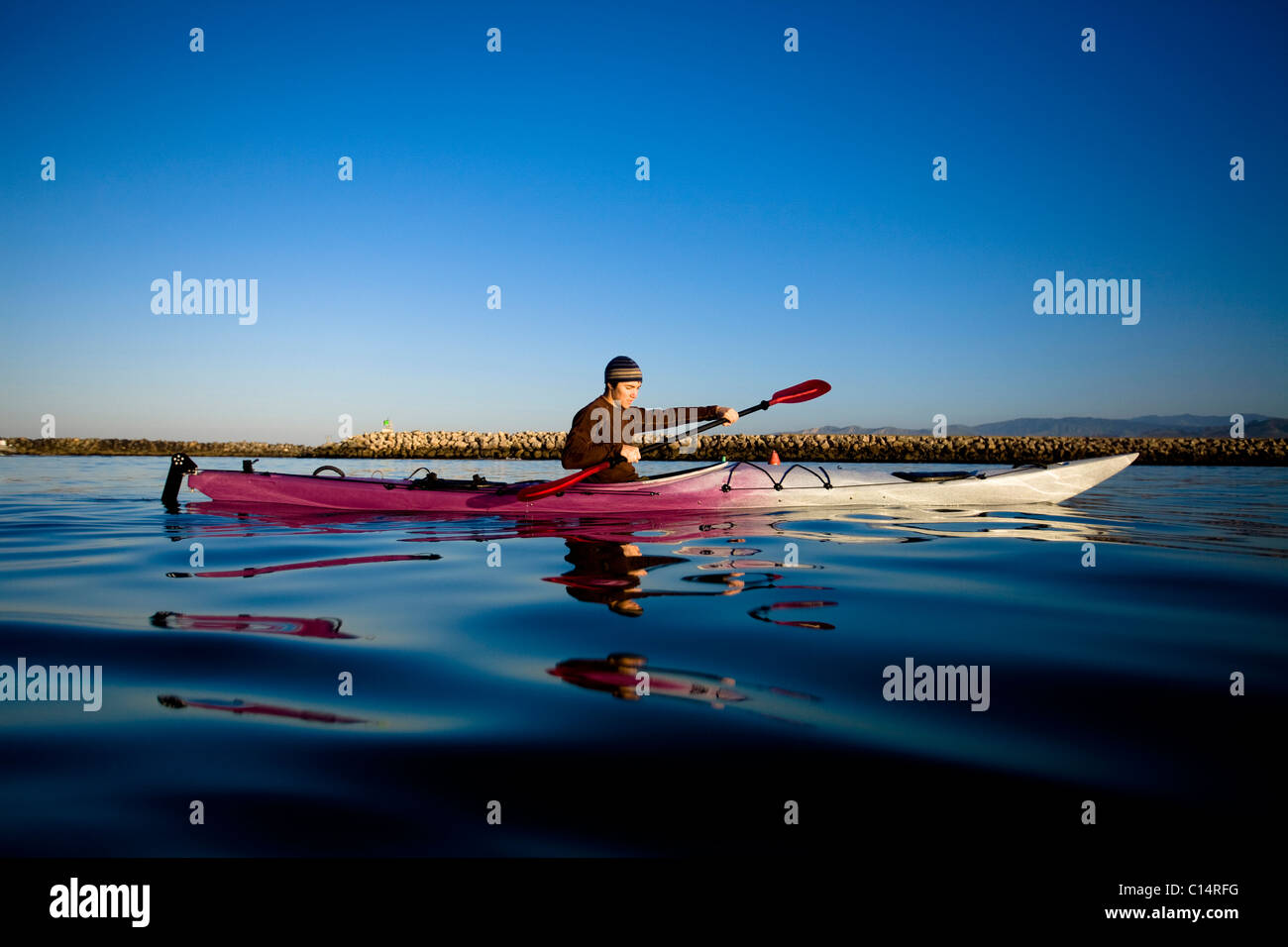 Un giovane uomo guarda alla sua riflessione mentre paddling una touring kayak appena al di fuori del porto di Ventura in Ventura. Foto Stock