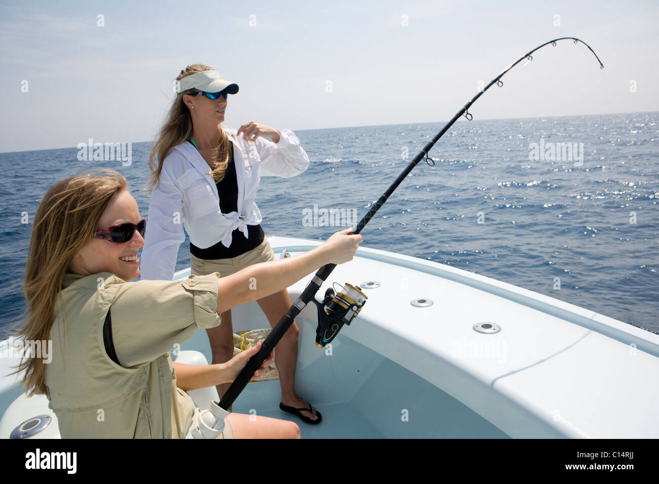 Due donne sono la pesca sulla prua di una barca con la piegatura dello stelo su una cattura. Foto Stock