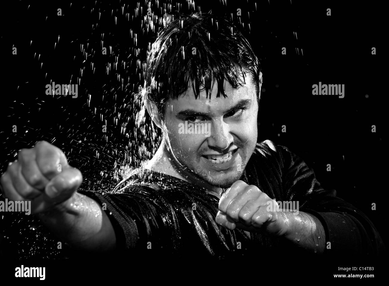 Un giovane uomo che indossa una camicia pone in un atteggiamento di wushu mentre piove giù su di lui. Foto Stock