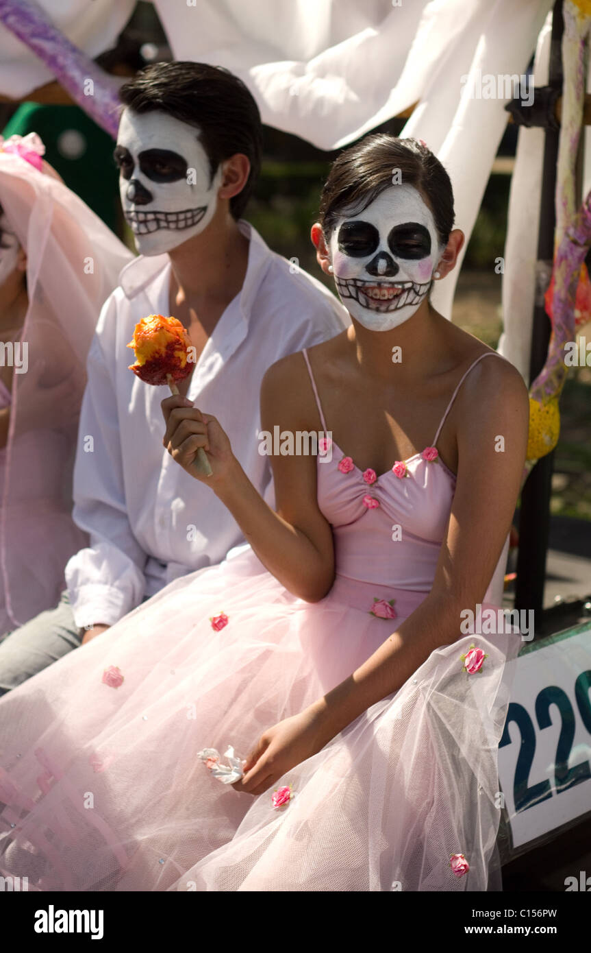 Mexican ballerini con scheletro make up, la ragazza è sempre sorridente e mangiando un mango con peperoncino dopo la sfilata di un corteo in città del Messico Foto Stock