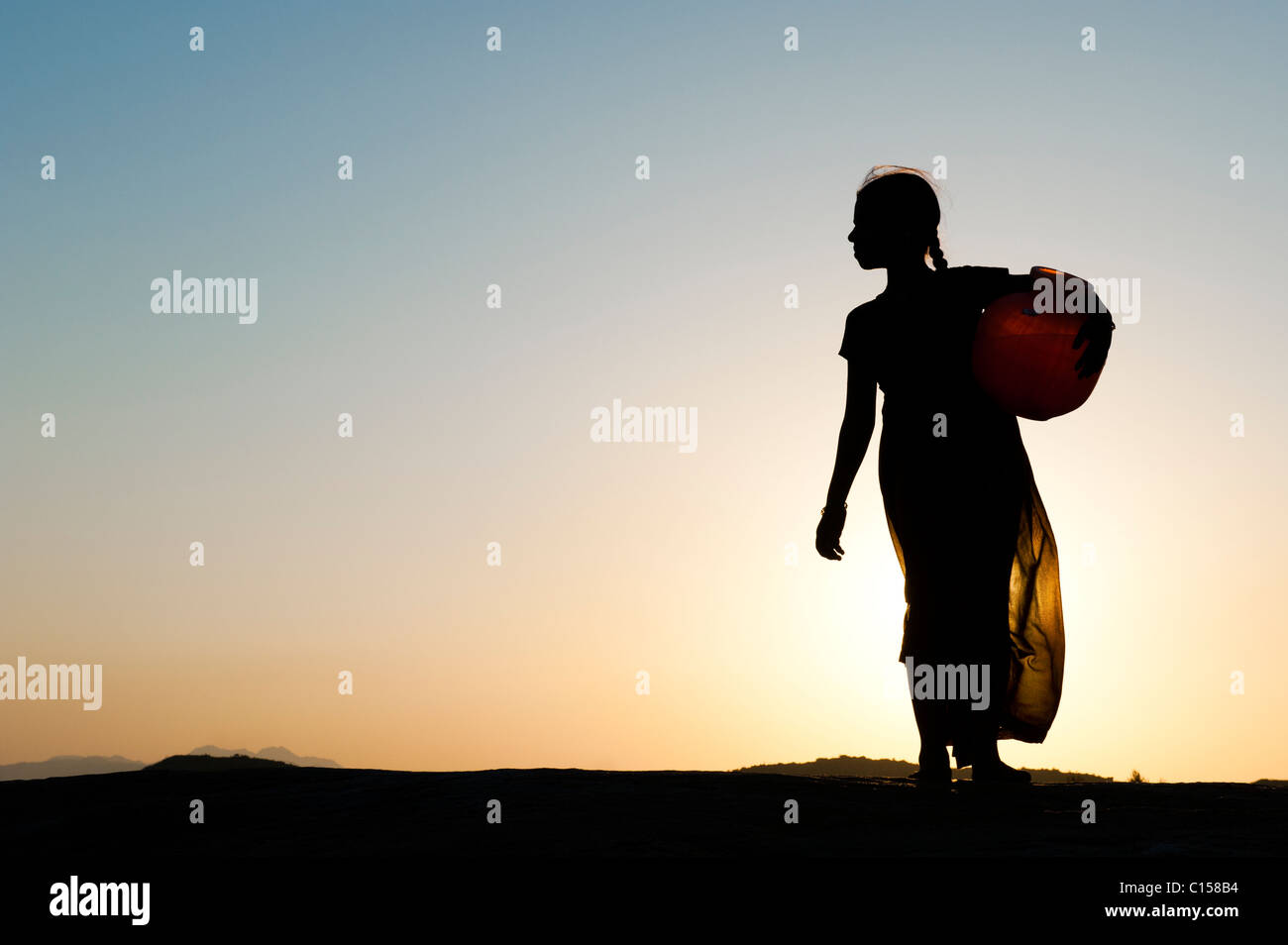 Rurale villaggio indiano ragazza che porta una pentola di acqua al tramonto. Silhouette. Andhra Pradesh, India Foto Stock