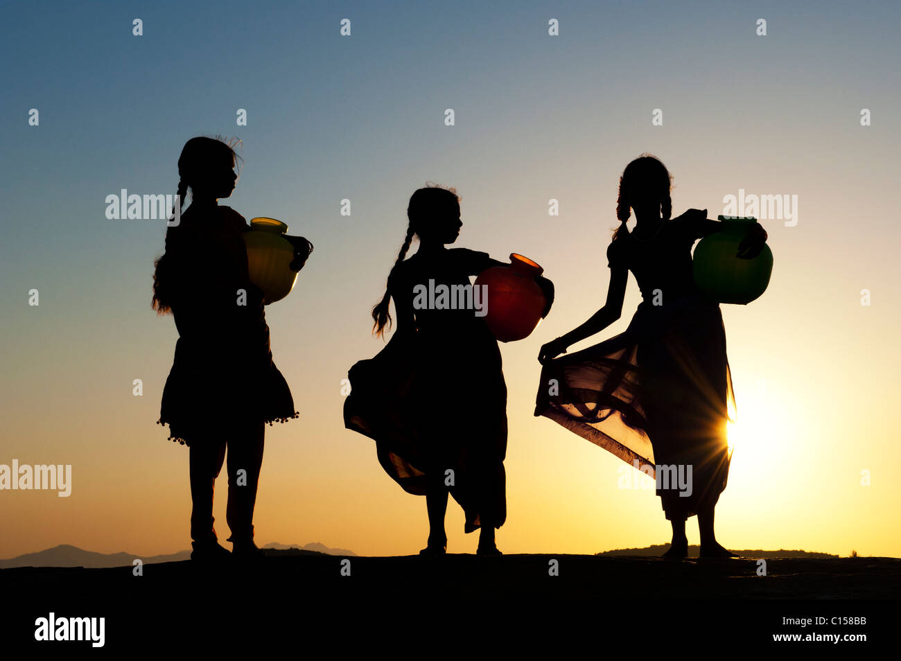 Rurale villaggio indiano ragazze con vasi d'acqua al tramonto. Silhouette. Andhra Pradesh, India Foto Stock
