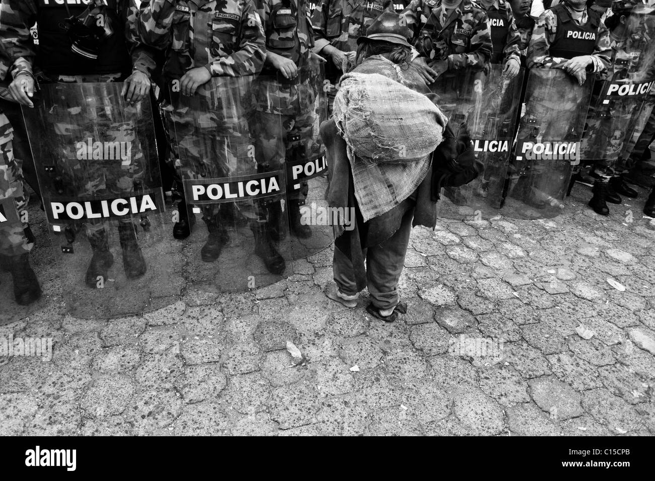 Un vecchio indiano Barefoot passa attraverso la Polizia antisommossa blocco durante il programma Inti Raymi (san juan) festeggiamenti in Cotacachi, Ecuador. Foto Stock