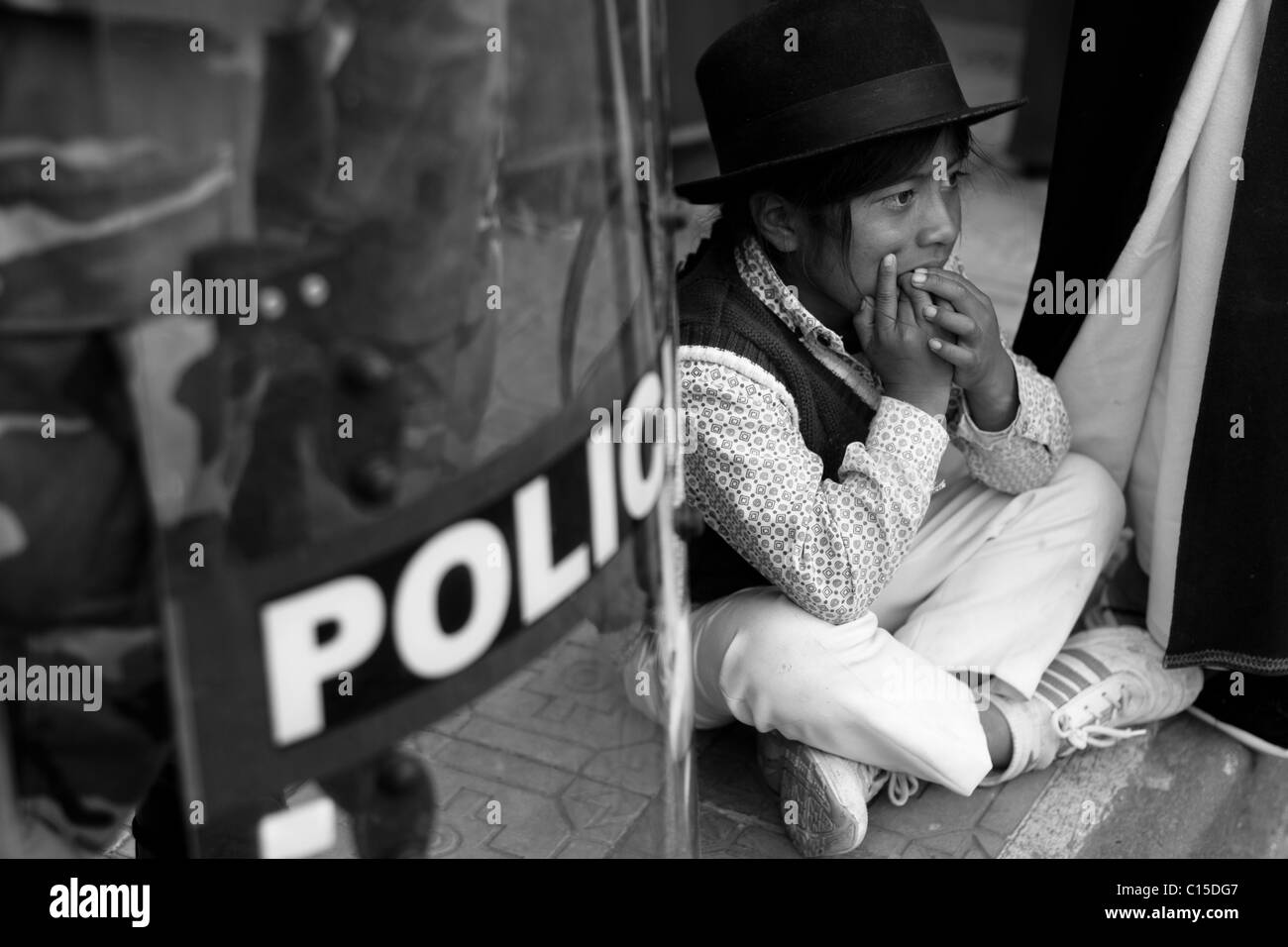 Un ragazzo indiano si siede sul marciapiede accanto a un poliziotto antisommossa durante l'Inti Raymi (san juan) festeggiamenti in Cotacachi, Ecuador. Foto Stock