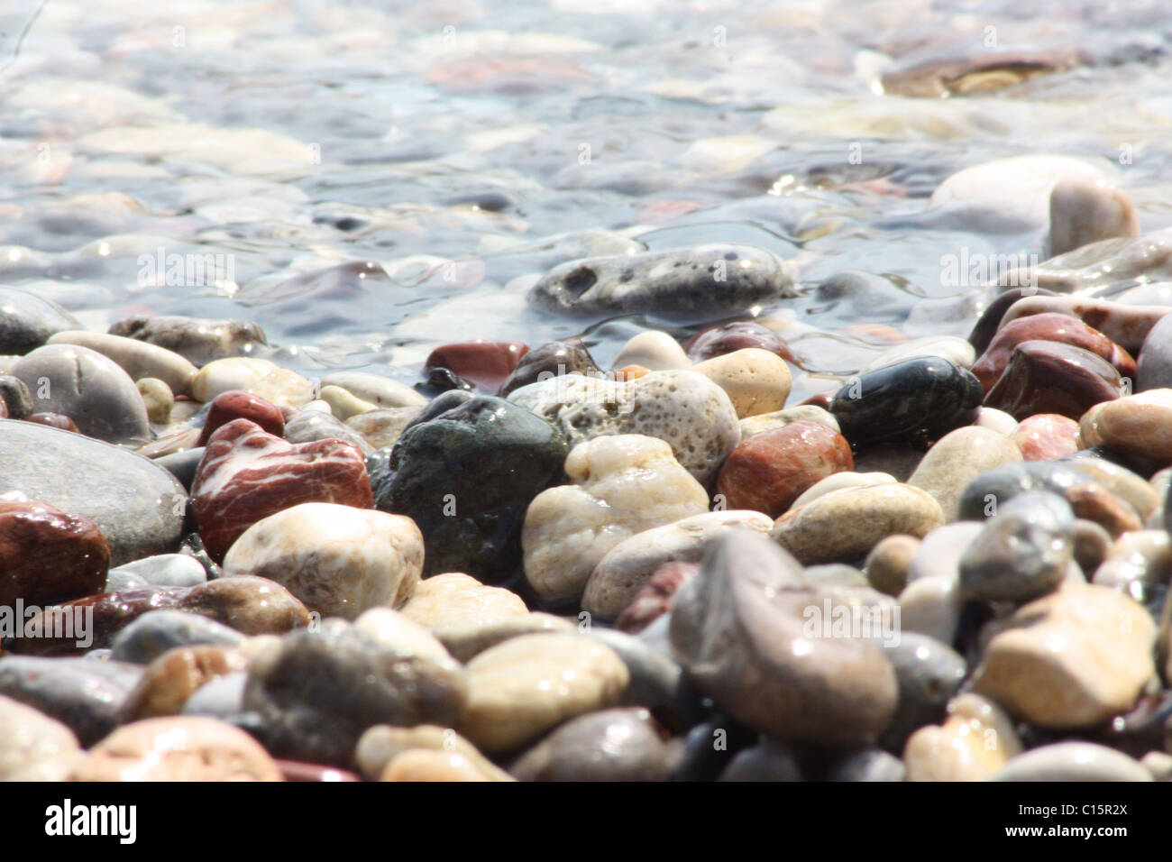 Soleggiato ciottoli bagnata sulla spiaggia con la marea che lambiscono dolcemente su di essi. Foto Stock