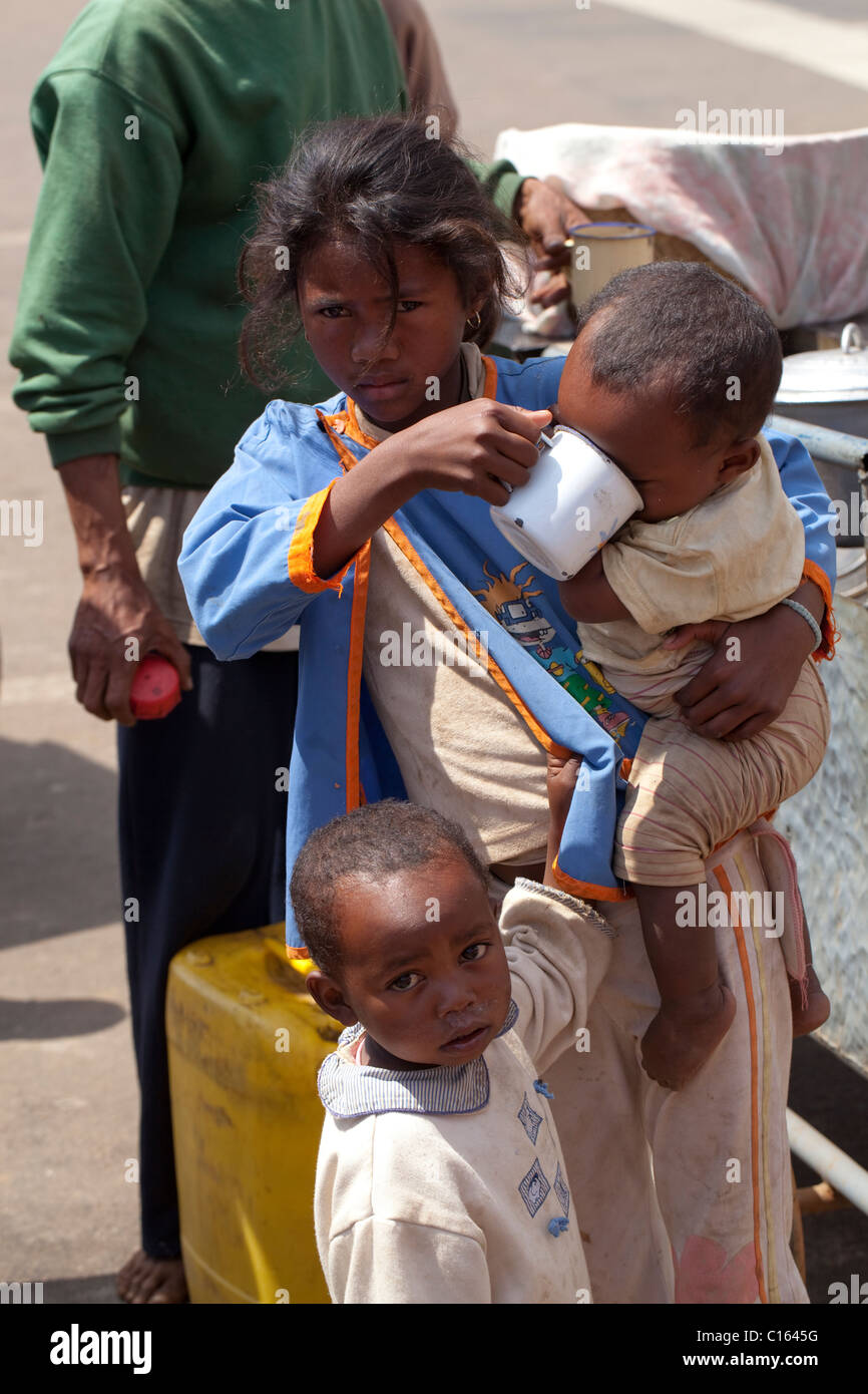 Ragazza avendo comprato acqua potabile per i gemelli fratelli più giovani. Toamasina o Tamatave. Regione di Atsinanana. Est del Madagascar. Foto Stock