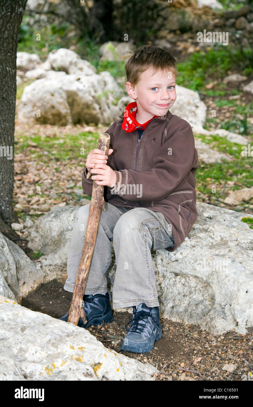 Il ragazzo, di sei anni di età, seduta in una radura con un bastone da passeggio Foto Stock