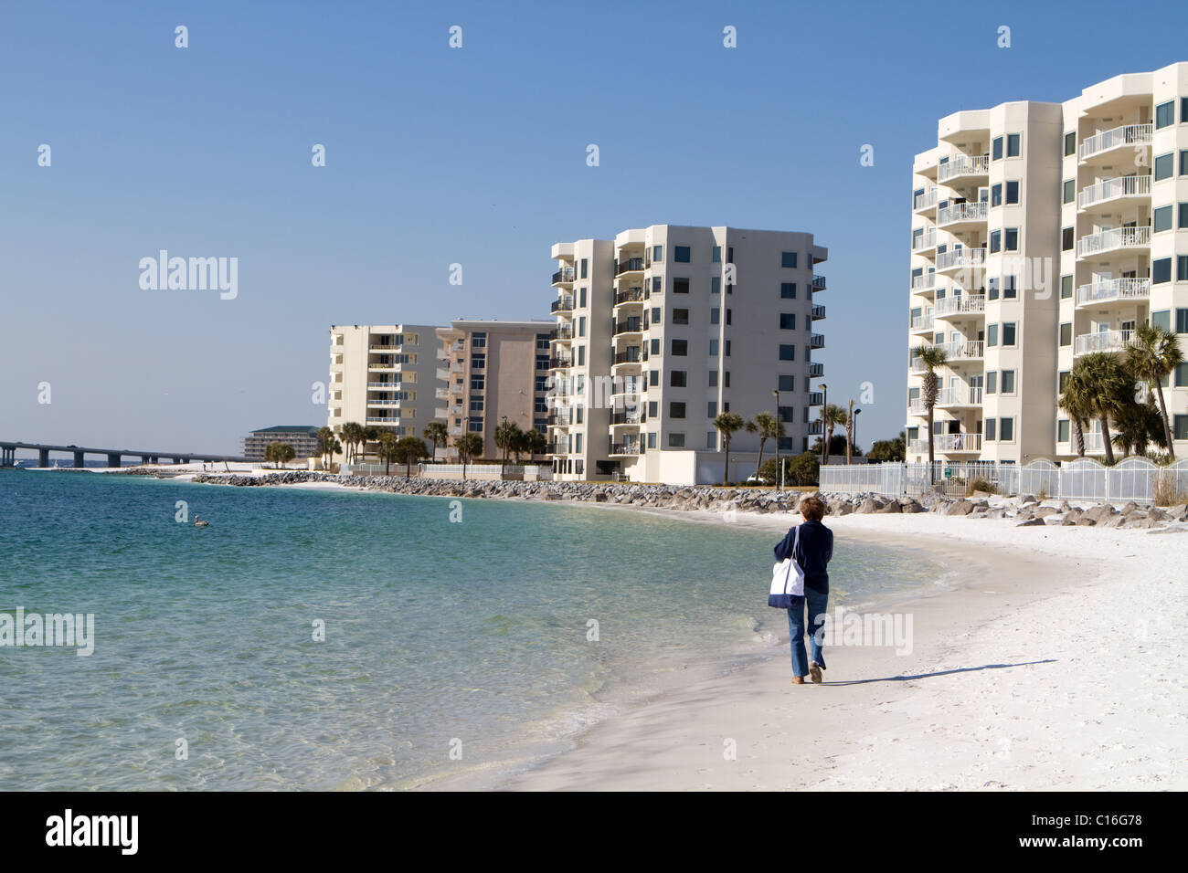 Femmina matura passeggiate turistiche lungo la spiaggia di fronte di condomini a Destin, in Florida. Foto Stock
