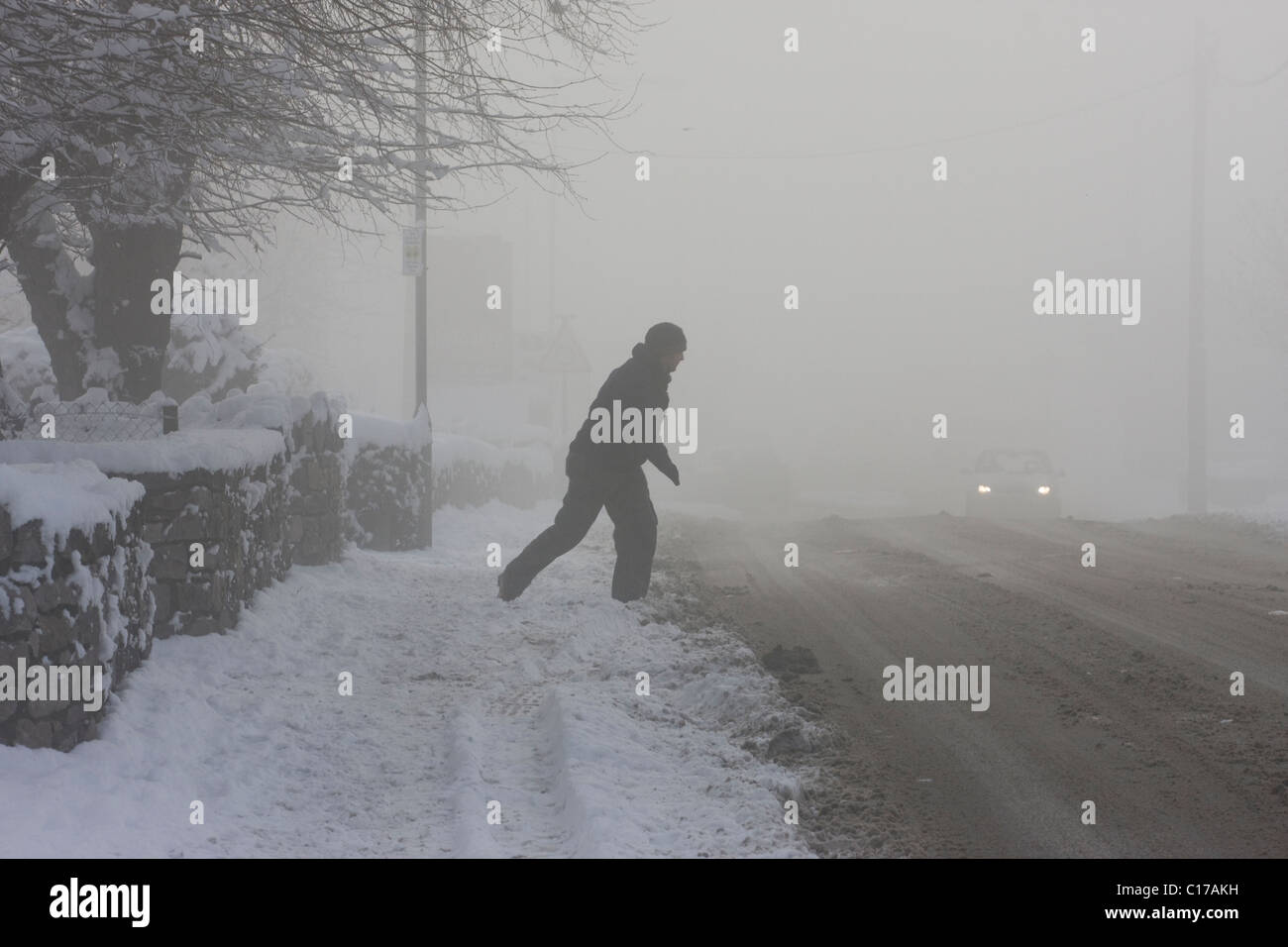 L'uomo della strada di attraversamento in condizioni meteorologiche pericolose ,il congelamento della nebbia e neve pesante Foto Stock