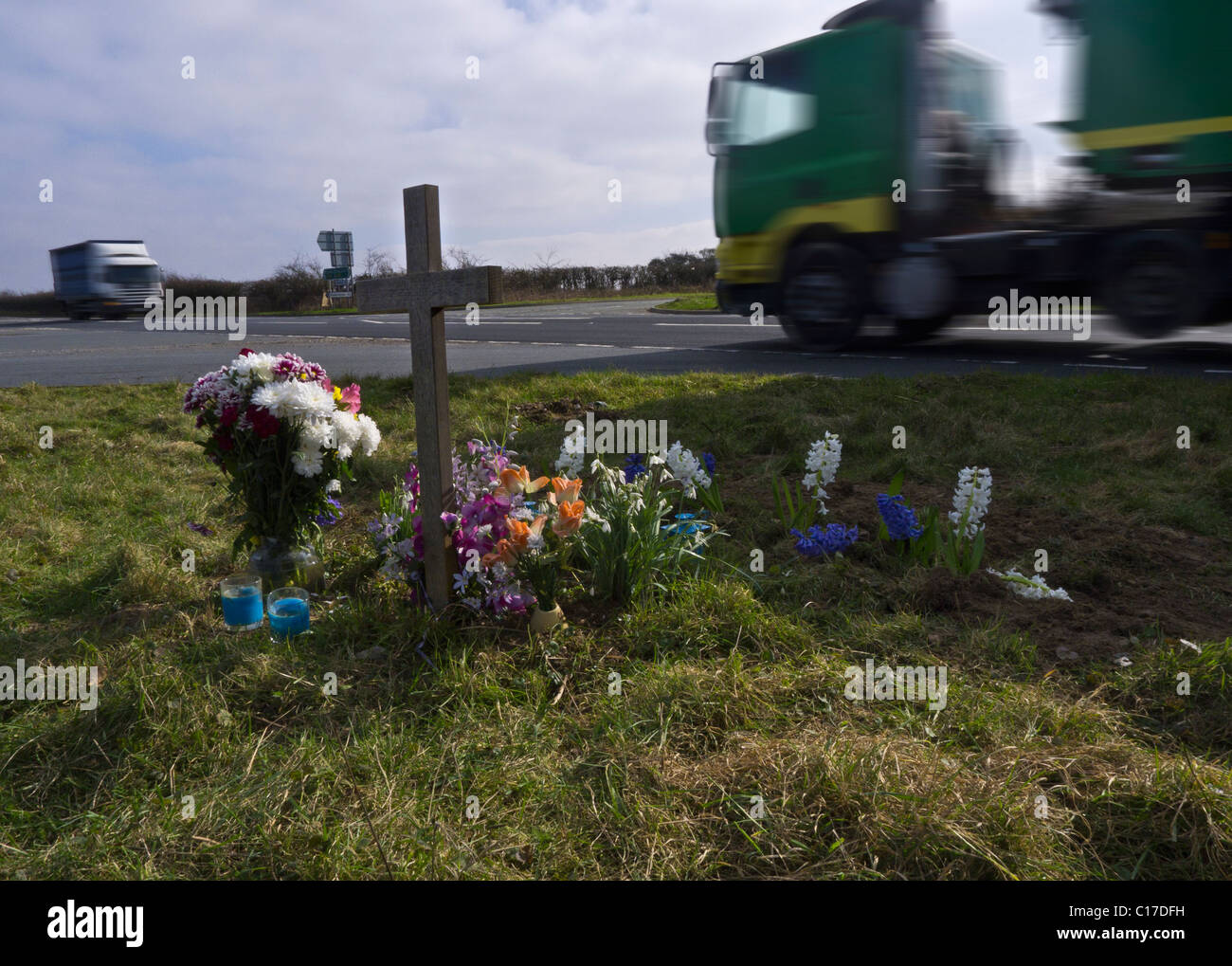 Mezzi pesanti passando un santuario di fortuna su una strada principale incidente blackspot. Foto Stock