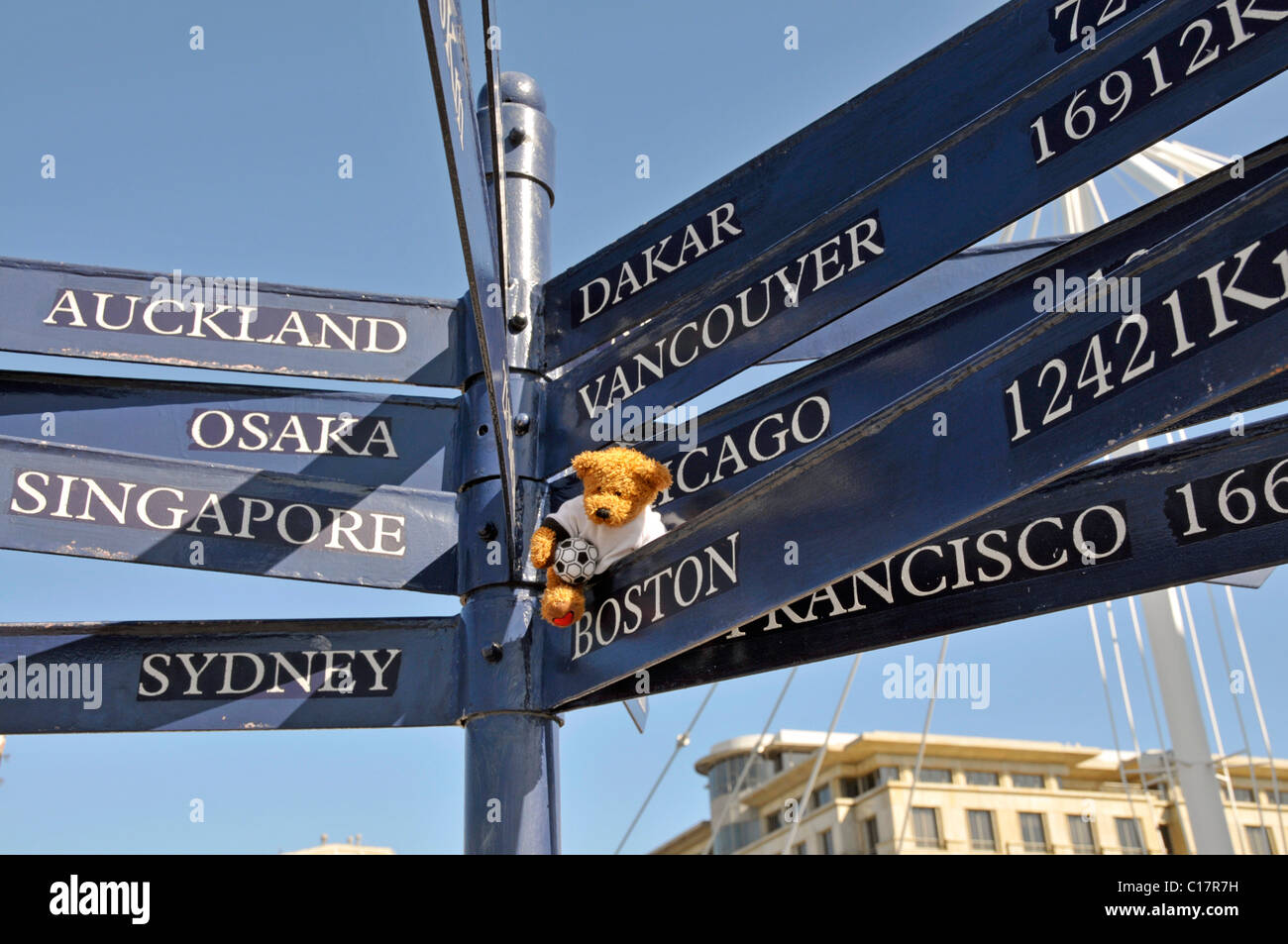 Orsacchiotto di peluche con un calcio su un cartello con distanze di varie città, il Waterfront, Città del Capo, Sud Africa Foto Stock