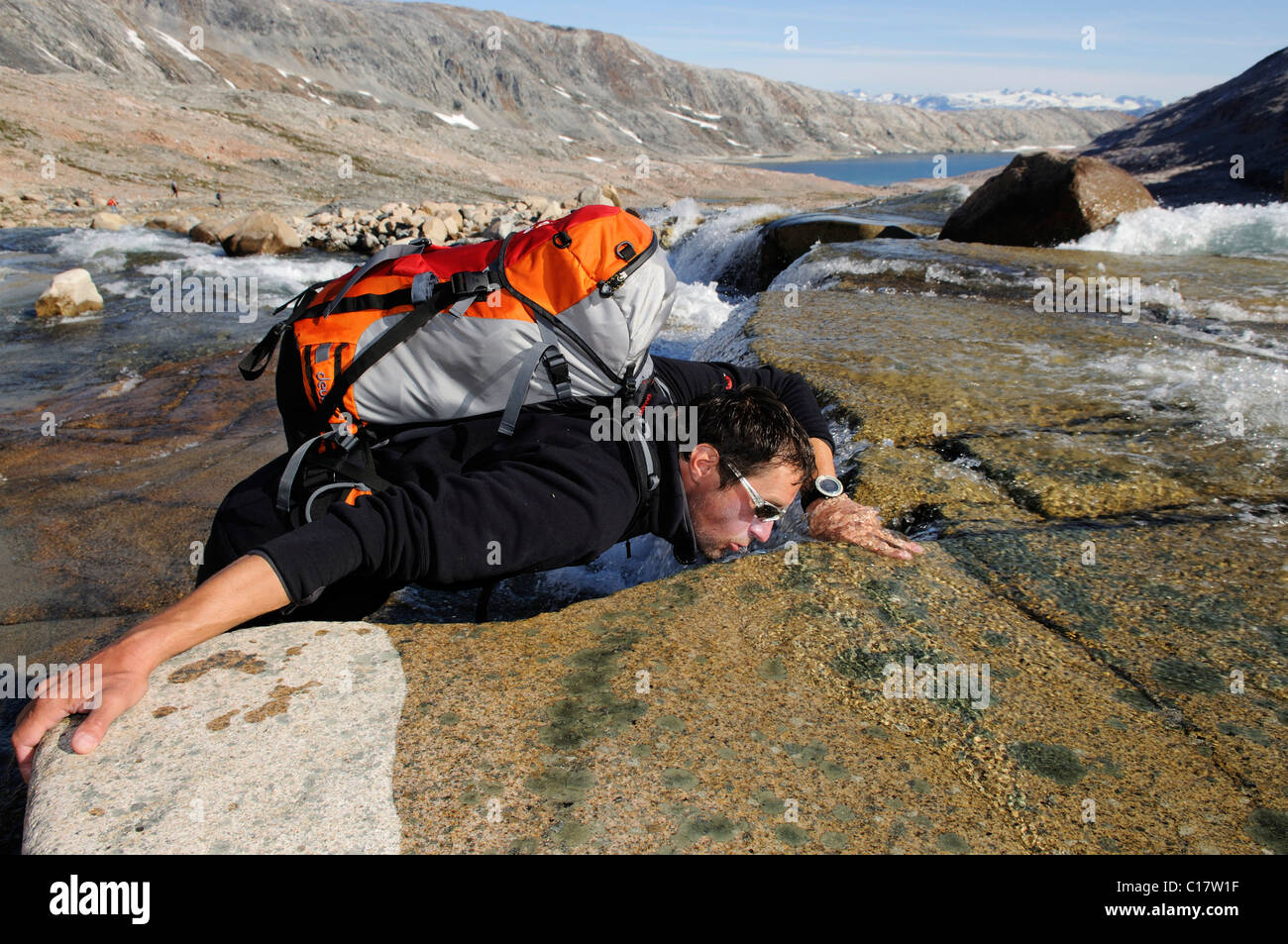 Un escursionista di bere da un torrente, Hundefjord, est della Groenlandia, Groenlandia Foto Stock