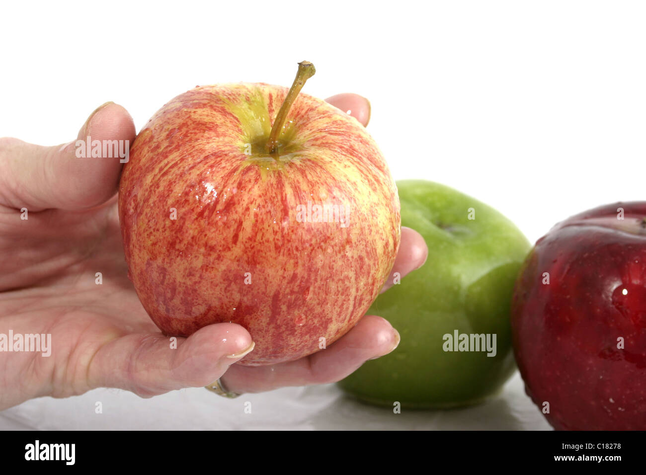 Mano che tiene una wet red apple con due mele, uno rosso e uno verde, in background. Foto Stock