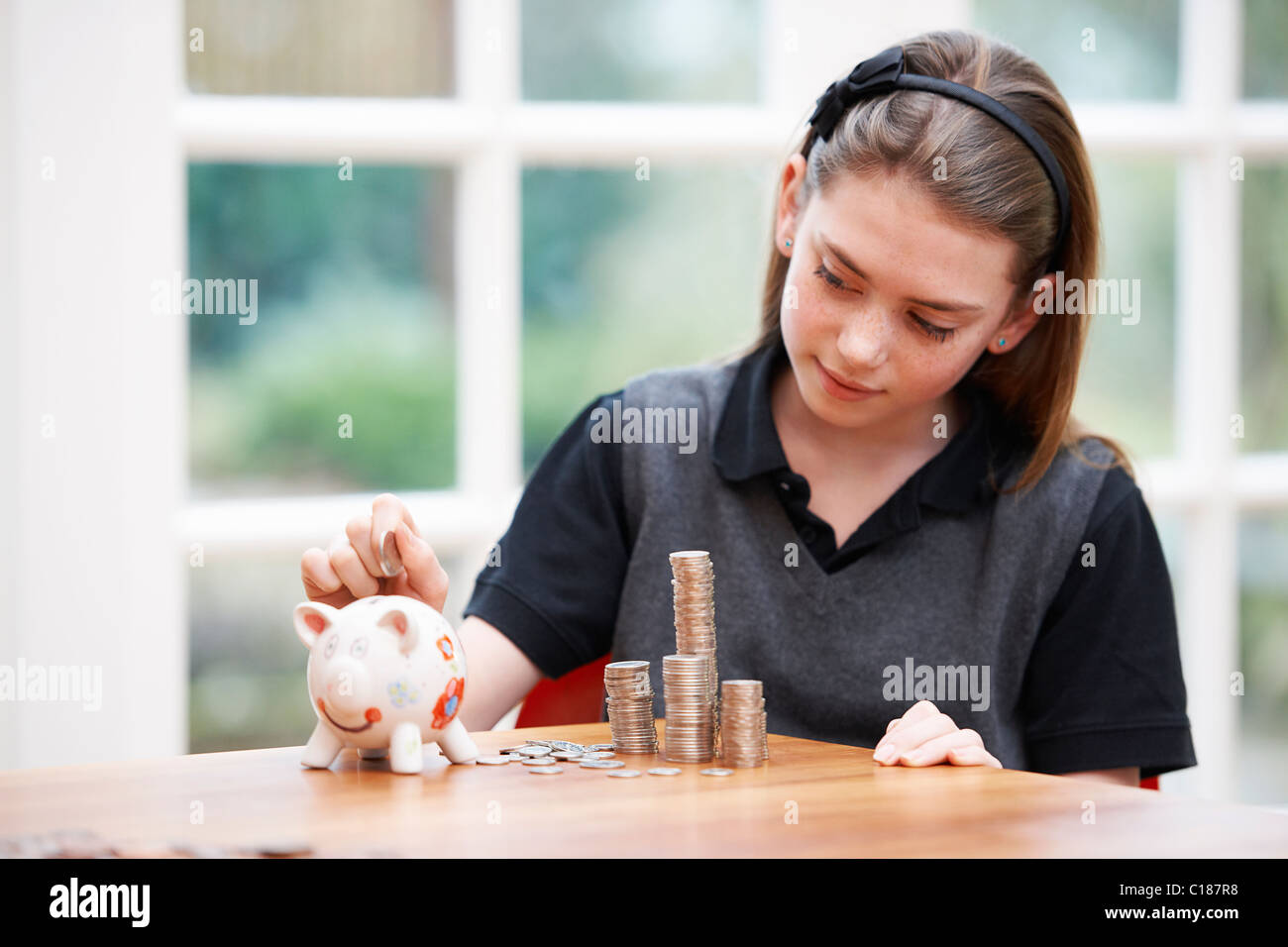 Ragazza con salvadanaio e pile di denaro Foto Stock