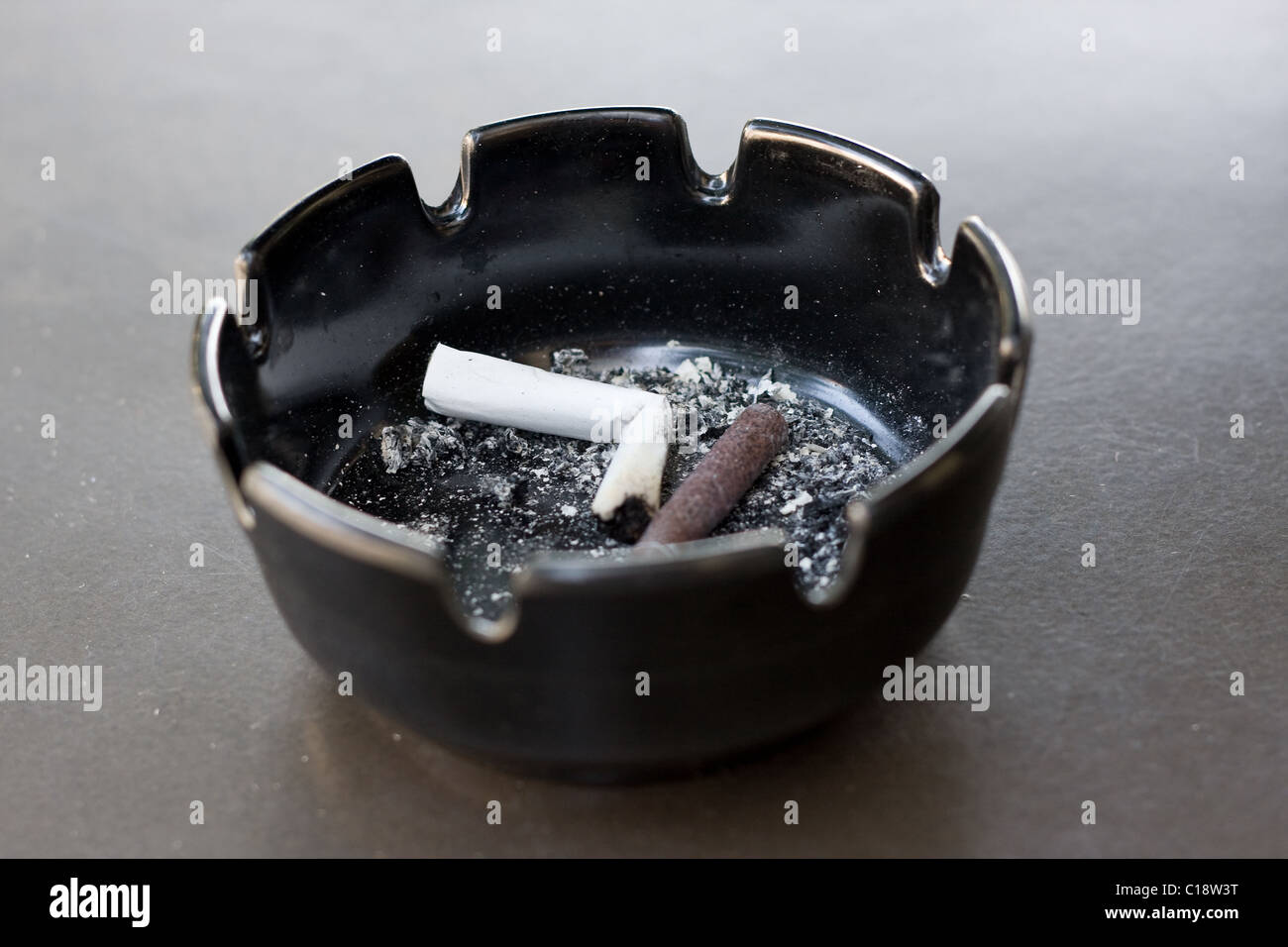 Sigarette e sigari e mozziconi di cenere in un posacenere su una tabella. Estremamente limitata profondità di campo con ceneri nel fuoco. Foto Stock