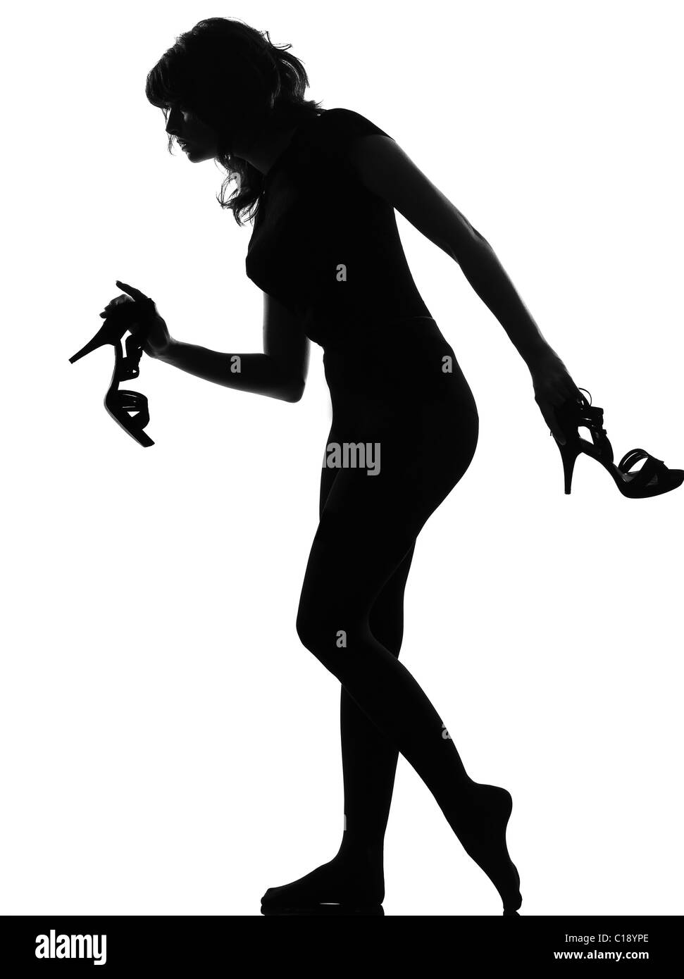 Silhouette in ombra di una giovane donna camminare molto a piedi nudi in punta di piedi tenendo alta scarpe tacco in studio su sfondo bianco Foto Stock