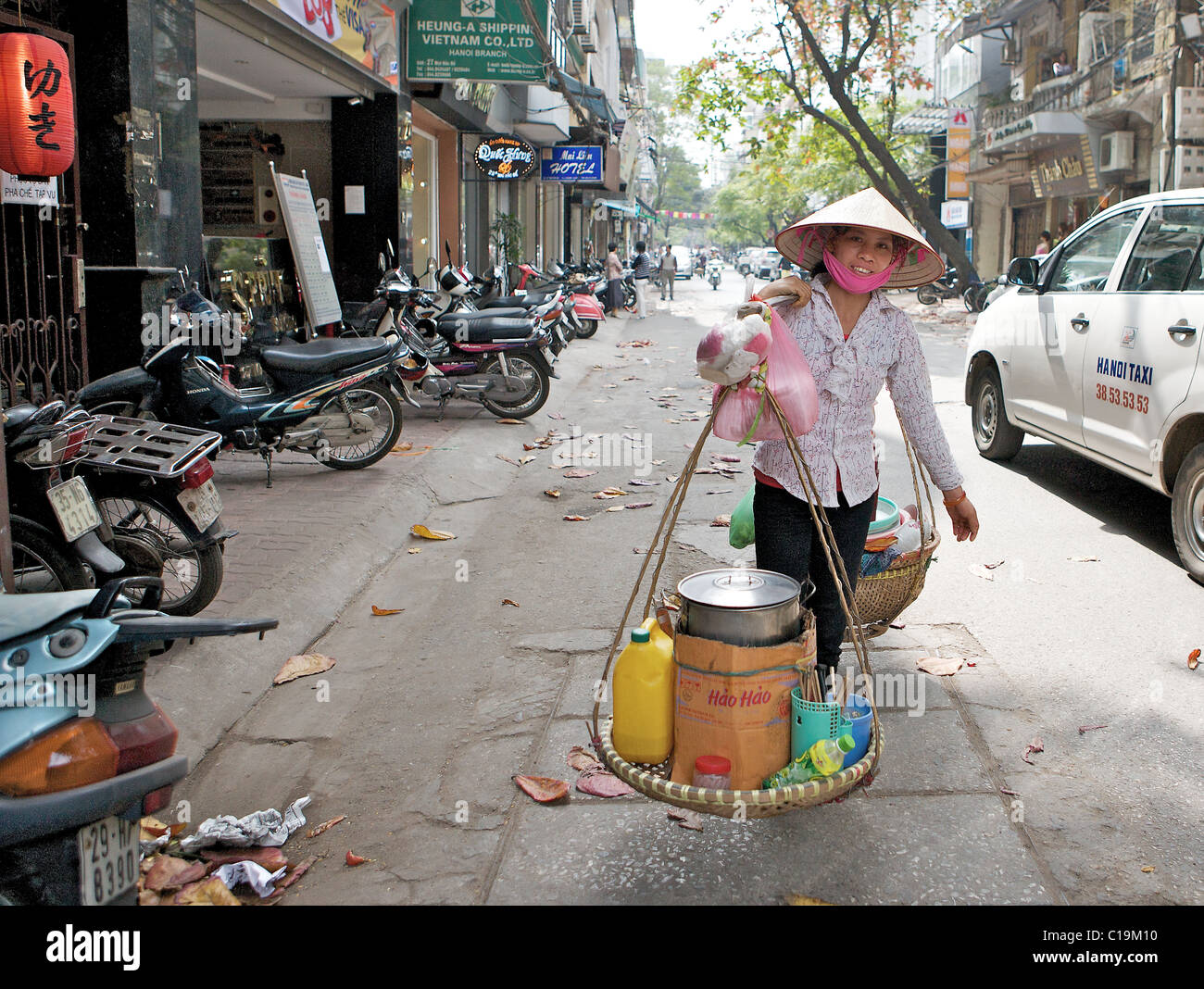 Una donna che porta una zuppa di mobile cucina e ristorante sul suo giogo lungo le strade di Hanoi, Vietnam Foto Stock