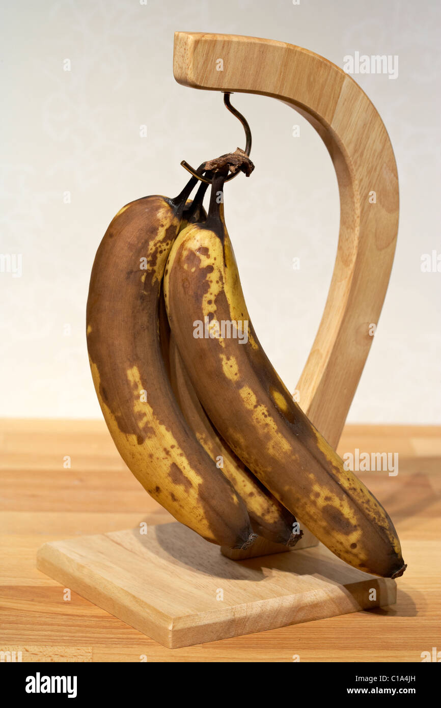 Banane stramature appeso ad una banana in legno appendiabiti Foto Stock