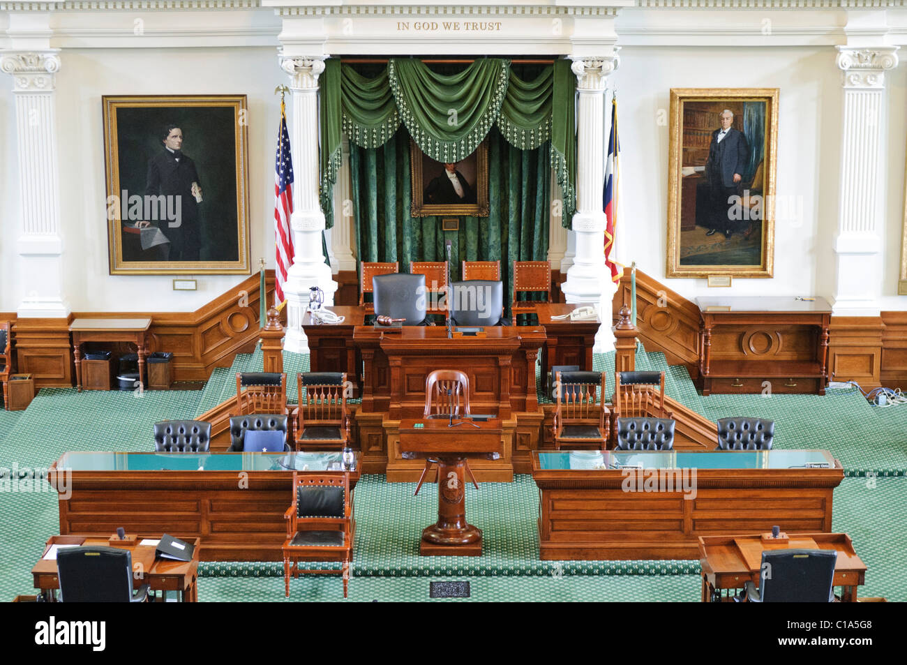 Tribuna presidenziale e scrivania del presidente della Camera del Senato del Capitolo dello Stato del Texas | AUSTIN, Texas — La tribuna presidenziale della Camera del Senato del Capitolo dello Stato del Texas, incisa con "In God We Trust" e ricoperta di damasco verde, si trova di fronte ai 31 scrivanie dei senatori su un pavimento ricoperto da un tappeto verde. Il vicegovernatore, che non è un membro eletto del Senato, presiede la Camera e detiene ampi poteri di nomina, rendendo l’incarico uno dei più influenti nel governo del Texas. Foto Stock