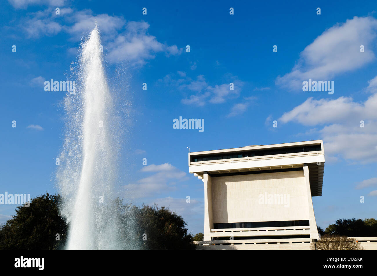 Biblioteca e Museo LBJ con Fontana Austin Texas | AUSTIN, Texas — Un alto getto d’acqua si innalza accanto alla Biblioteca e al Museo LBJ, il cui spruzzo quasi eguaglia l’altezza della torre brutalista rivestita in travertino di Gordon Bunshaft nel campus dell’Università del Texas. Dedicato nel 1971 e gestito dall’National Archives and Records Administration, l’edificio ospita circa 45 milioni di pagine di documenti della presidenza Johnson, rendendolo una delle collezioni più estese nel sistema delle biblioteche presidenziali. Foto Stock