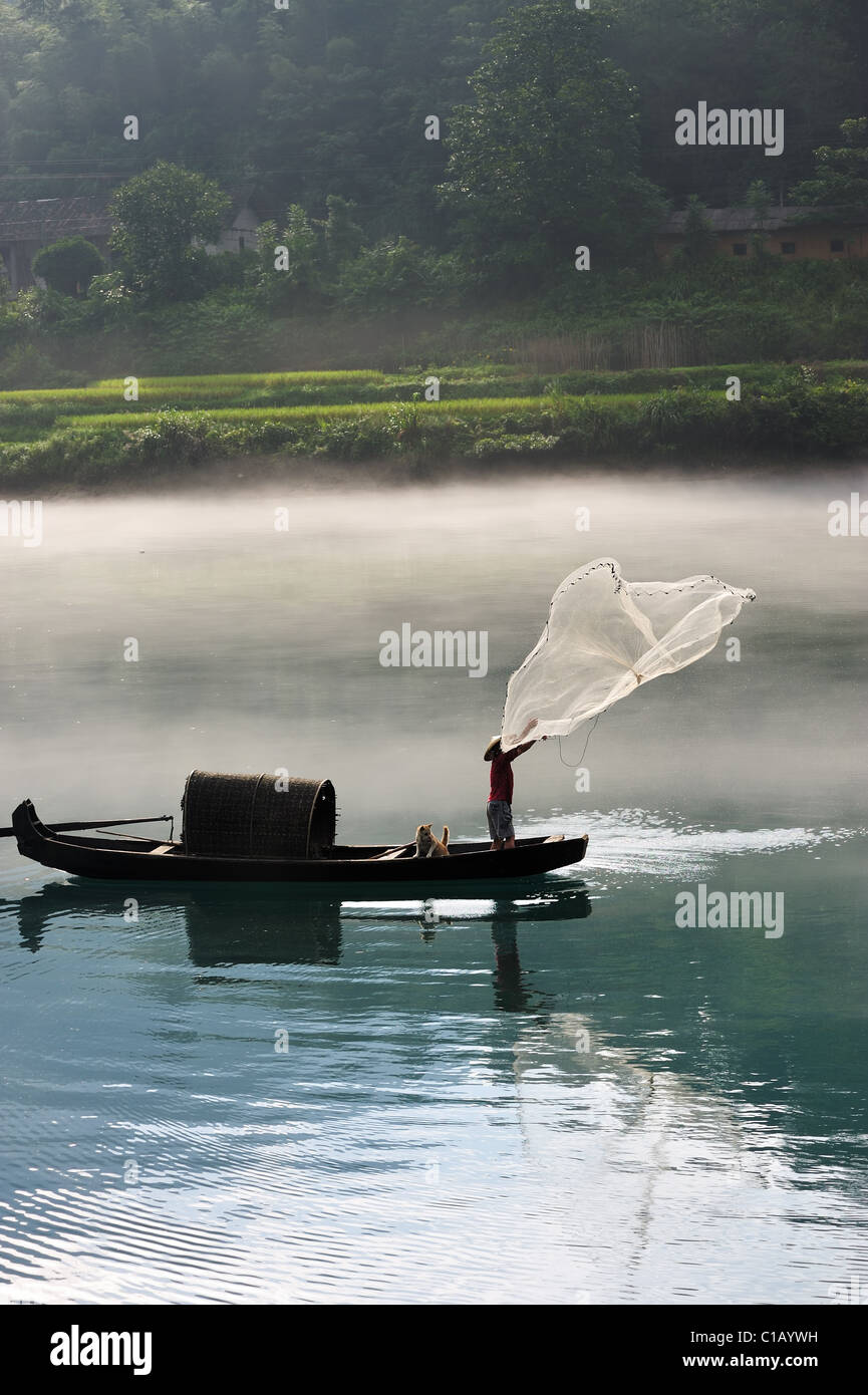 Un pescatore di fusione il suo net dalla barca sul fiume Foto Stock