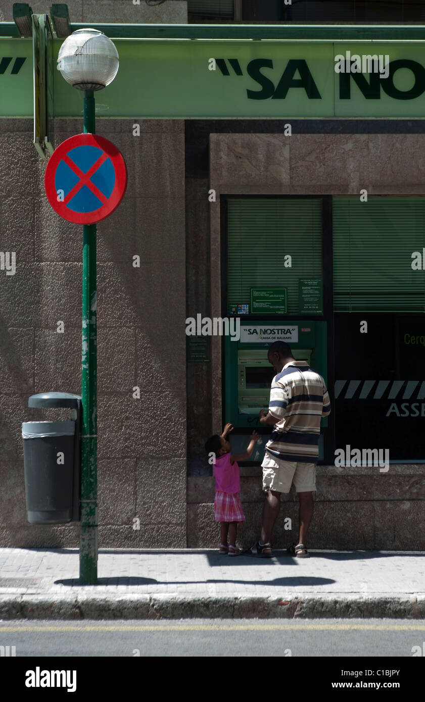 Uomo padre con la figlia bambino usando 'ATM cash dispenser' 'Sun' nosta banca strada in Palma de Maiorca Spagna Foto Stock