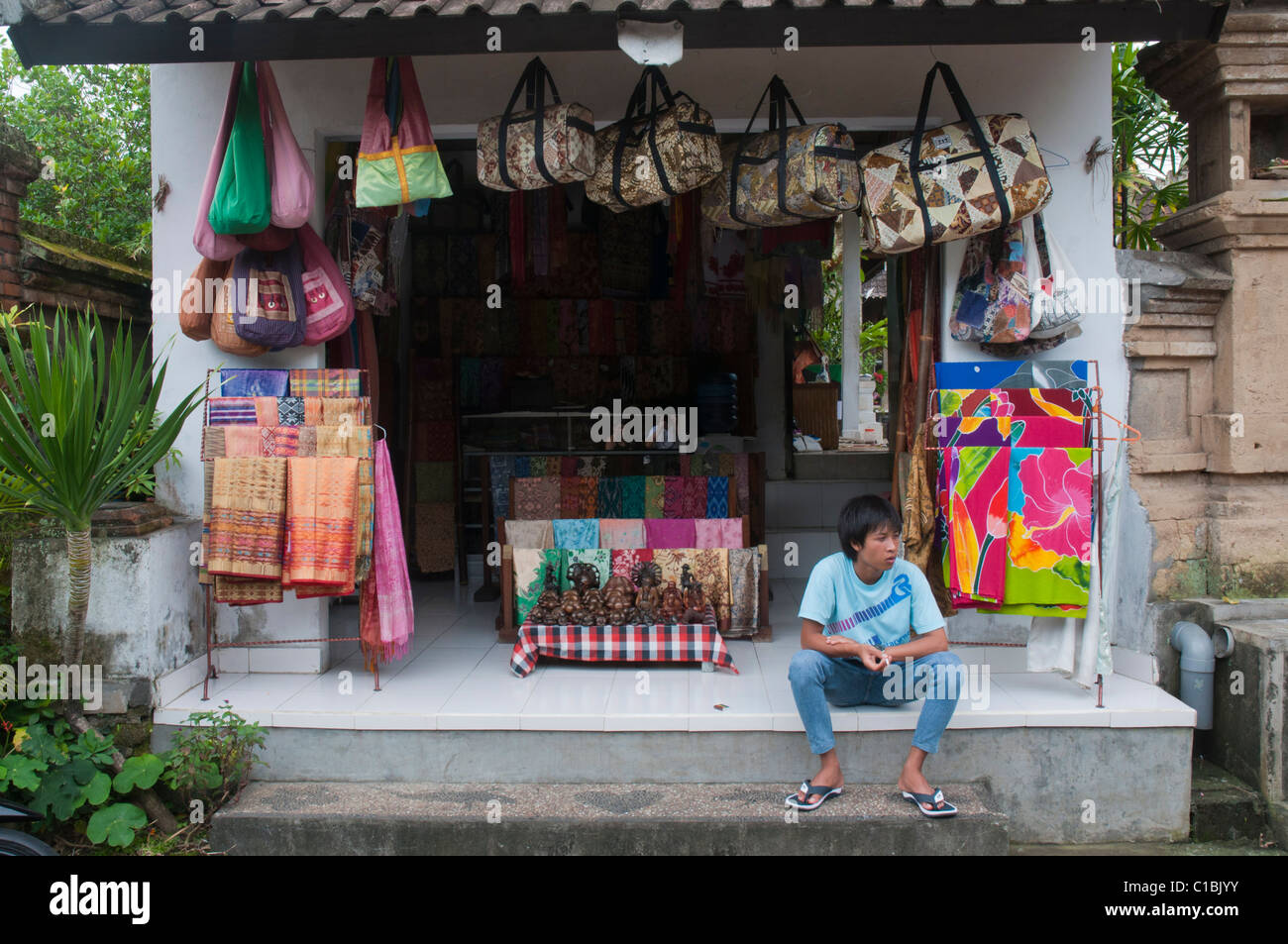 Una gioventù seduta al di fuori di un negozio di souvenir in Ubud, Bali Indonesia Foto Stock