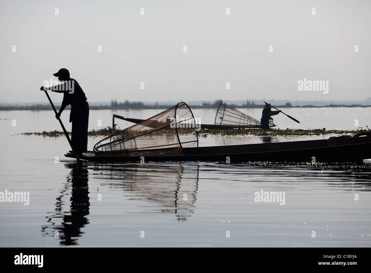 Ammaliante tribal pescatore sul Lago Inle in Birmania. Singolare tecnica di gamba-barca a remi e coniche Tutina in rete. Foto Stock