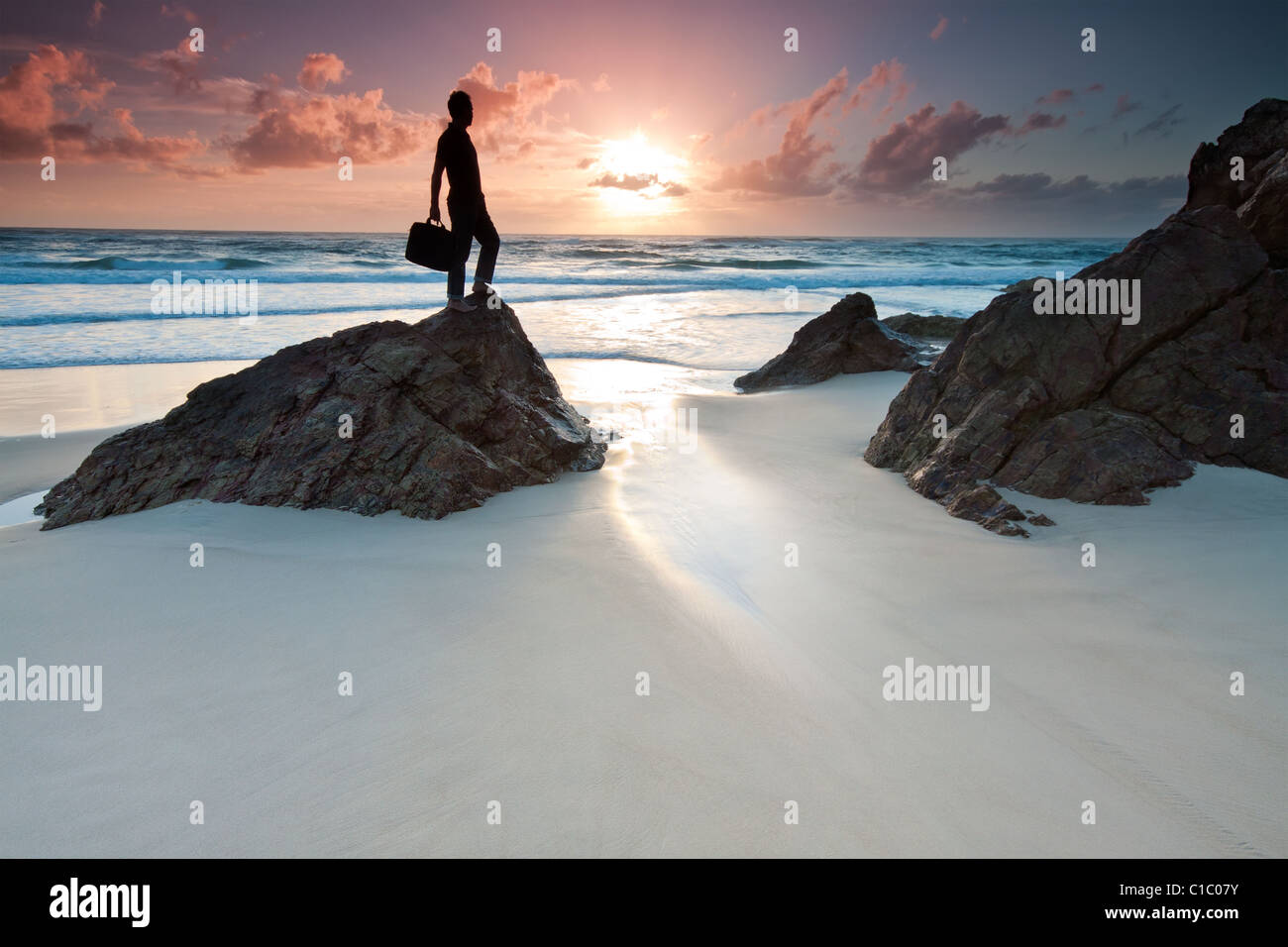 L uomo è tenendo il suo computer portatile del sacco quando è in piedi sulla sommità della roccia a sunrise (miami beach,Queensland, Australia) Foto Stock