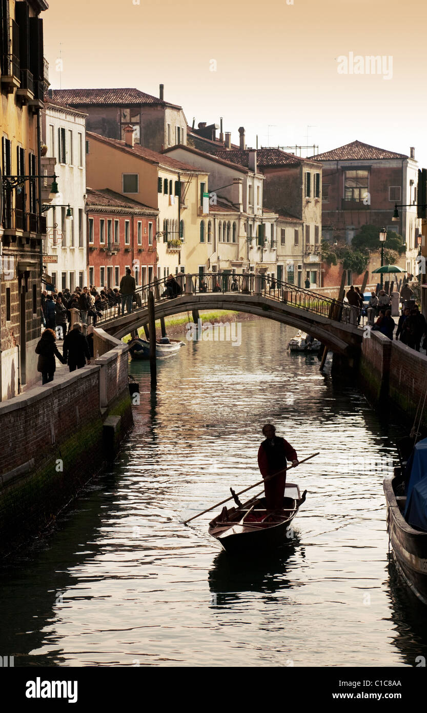 Un barcaiolo guida la sua barca lungo un canale al tramonto, Venezia, Italia Foto Stock