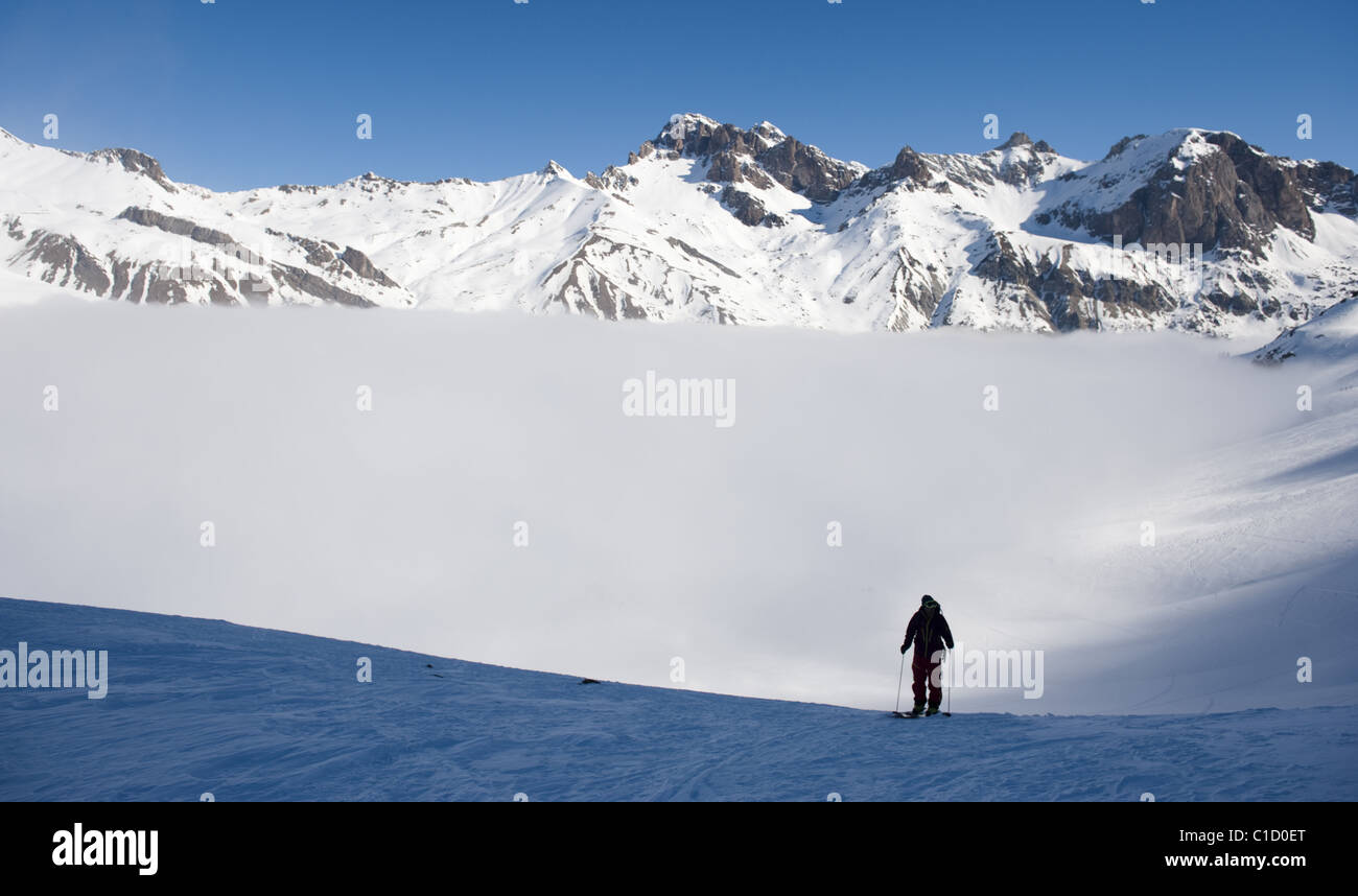 Un uomo a scalare una montagna innevata lato con pelli di arrampicata su i suoi sci al Col du Lautaret, vicino La Grave, Francia. Foto Stock