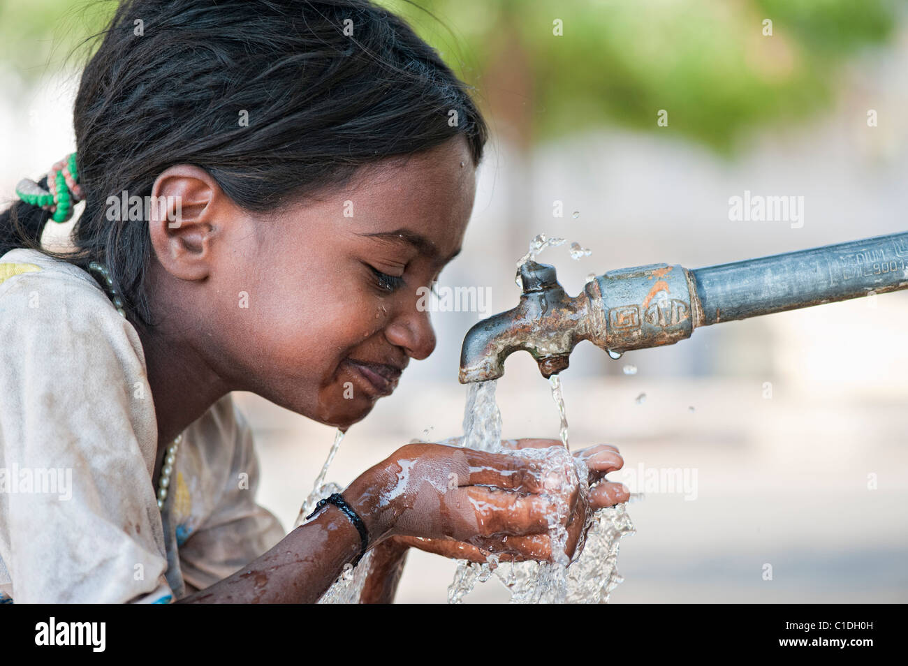 I giovani poveri di casta inferiore ragazza indiana di bere da un rubinetto di acqua. Andhra Pradesh, India Foto Stock