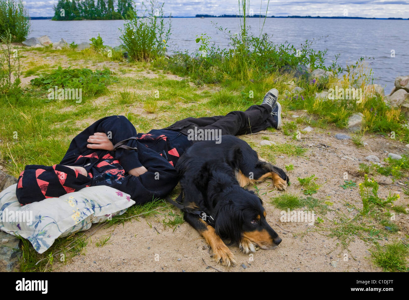 Ragazzo adolescente e il suo cane giacenti presso il lago Hjalmaren in Svezia. Foto Stock